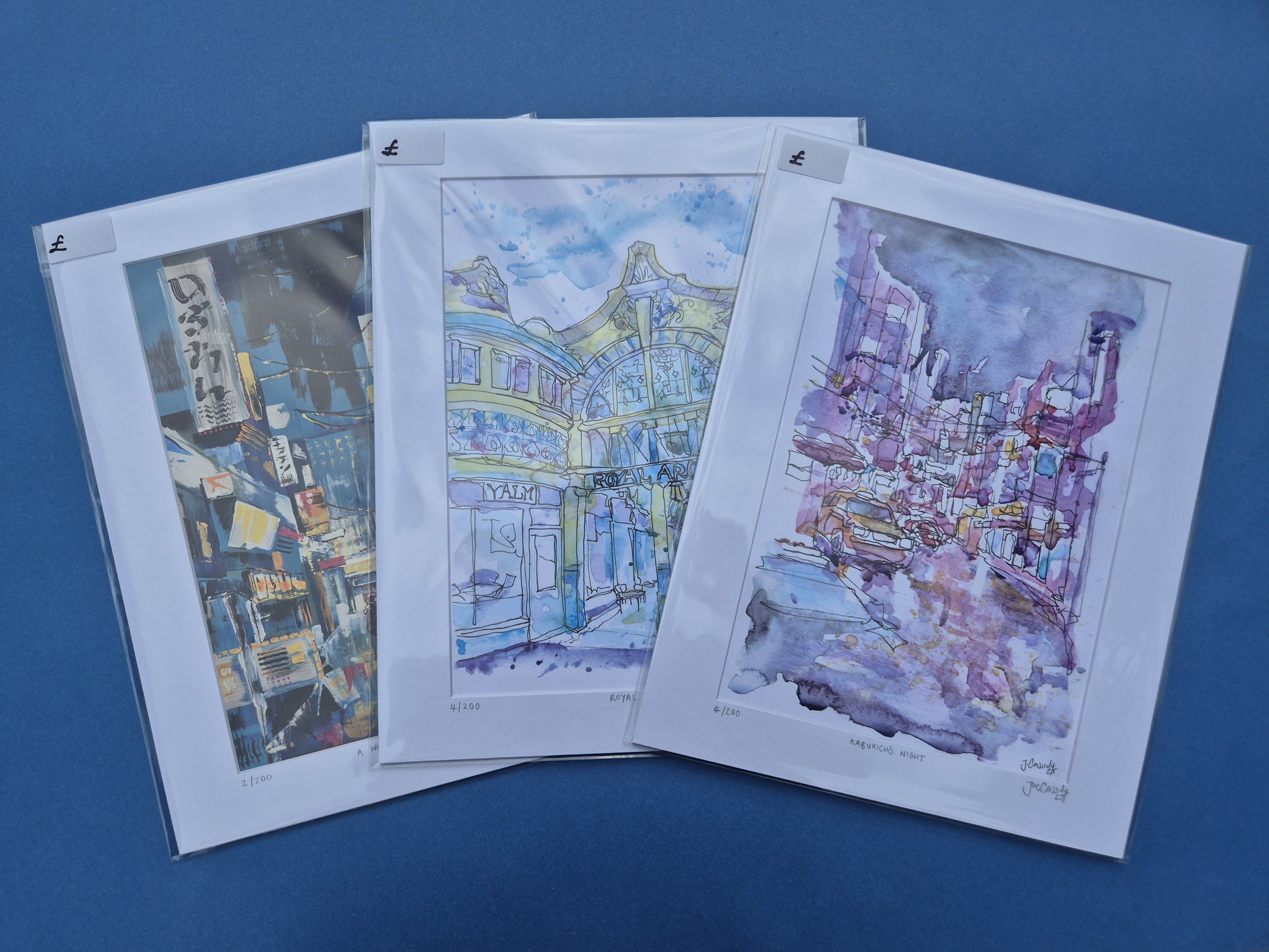 Three watercolour art prints of city scenes and architectural details, each numbered and signed, displayed against a blue background.