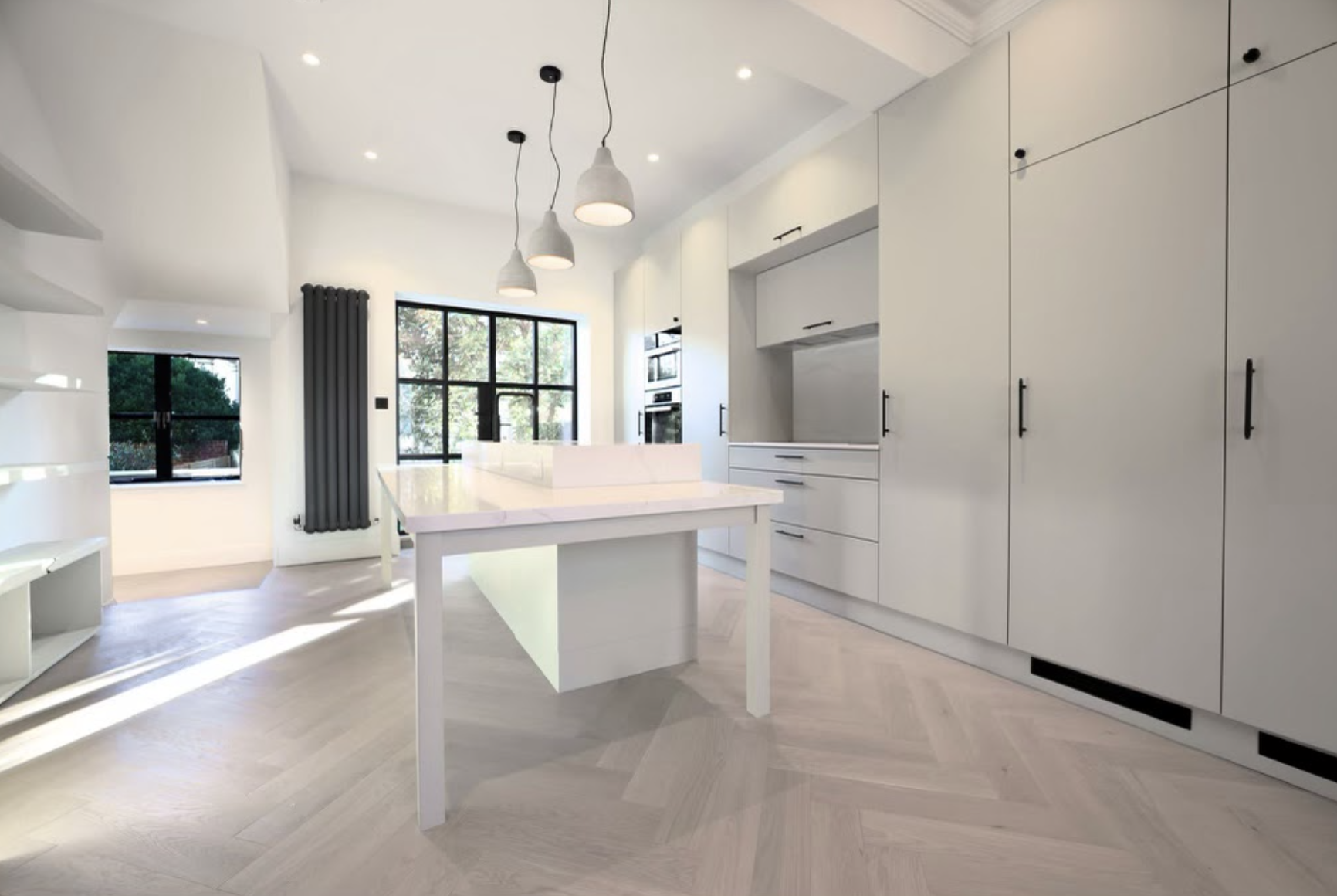 Contemporary kitchen with herringbone flooring, table-style island with integrated sink and Crittall doors opening onto a decked roof terrace