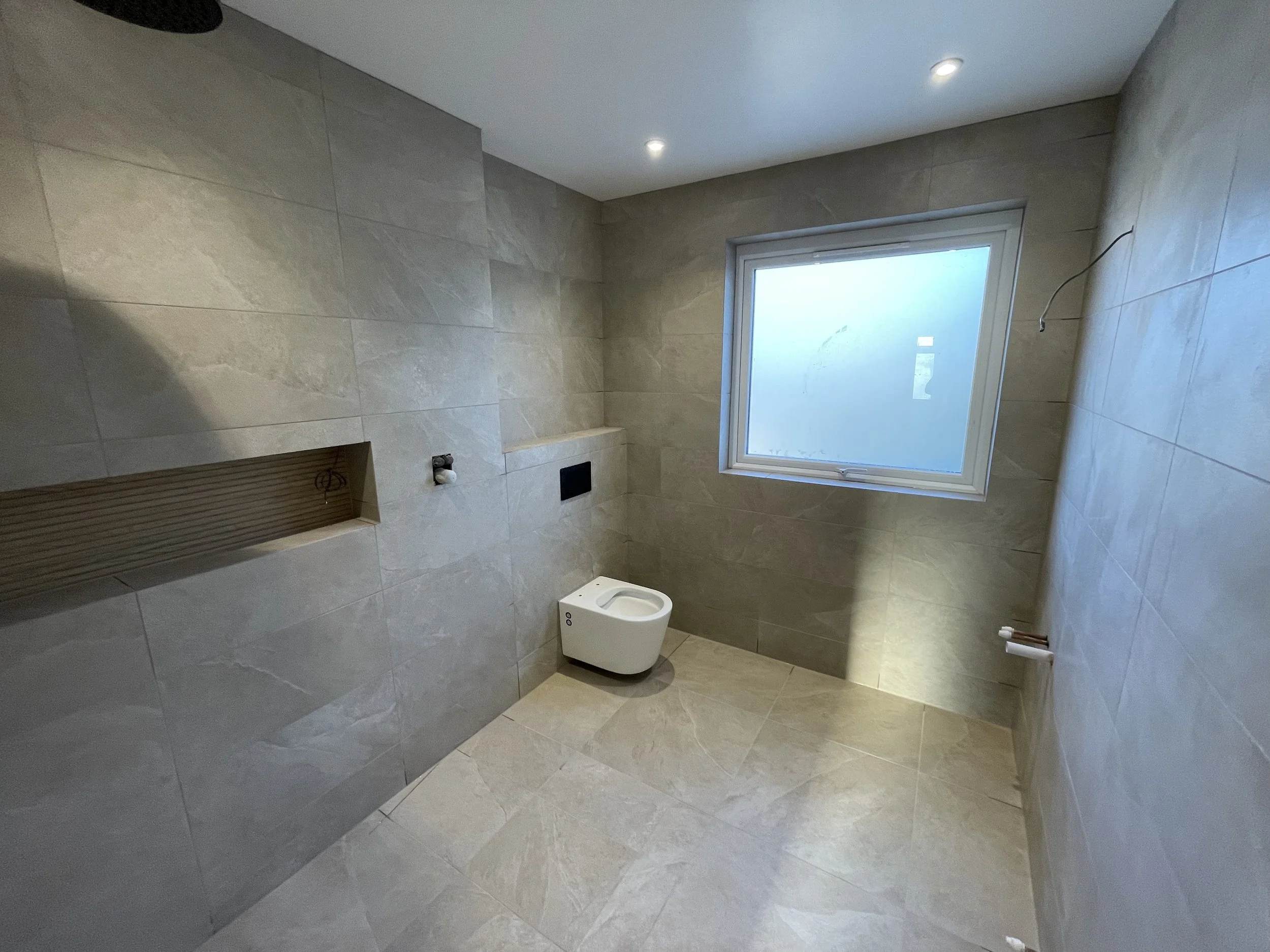 Large-format porcelain bathroom tiling with mitred corners, tiled niche, walk-in shower and wall-hung toilet