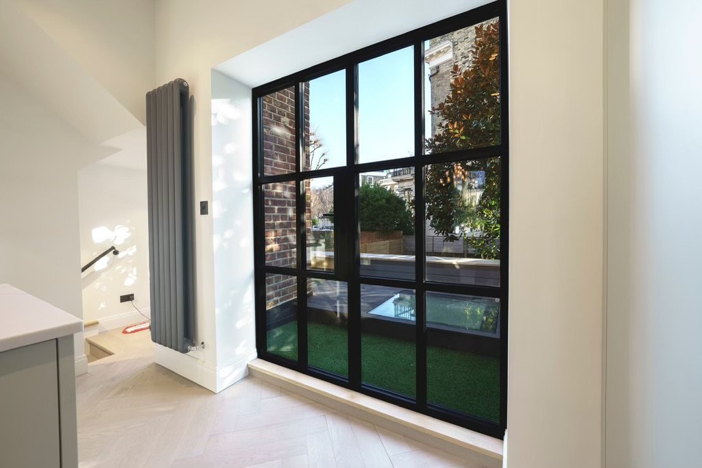 Renovated interior with Crittall doors, staircase and modern column radiator opening onto a decked roof terrace