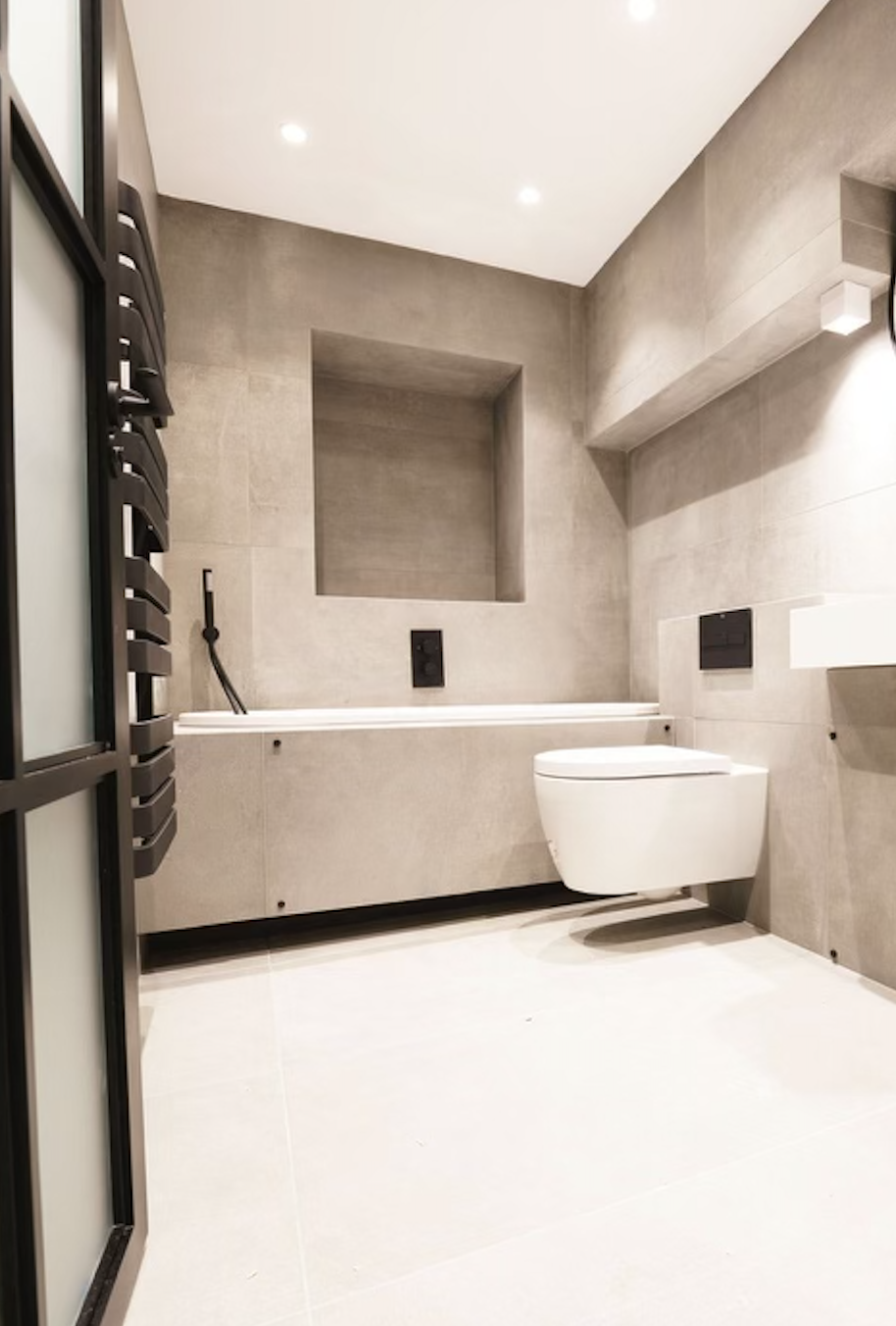 Contemporary bathroom with large-format grey porcelain tiles, sunken bath, tiled sanitaryware, mitred edges and black fixtures