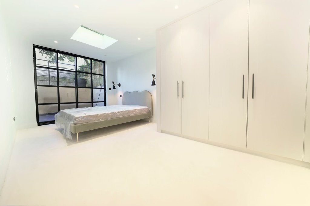 Renovated bedroom with built-in wardrobes, skylight and Crittall door opening onto a decked garden area