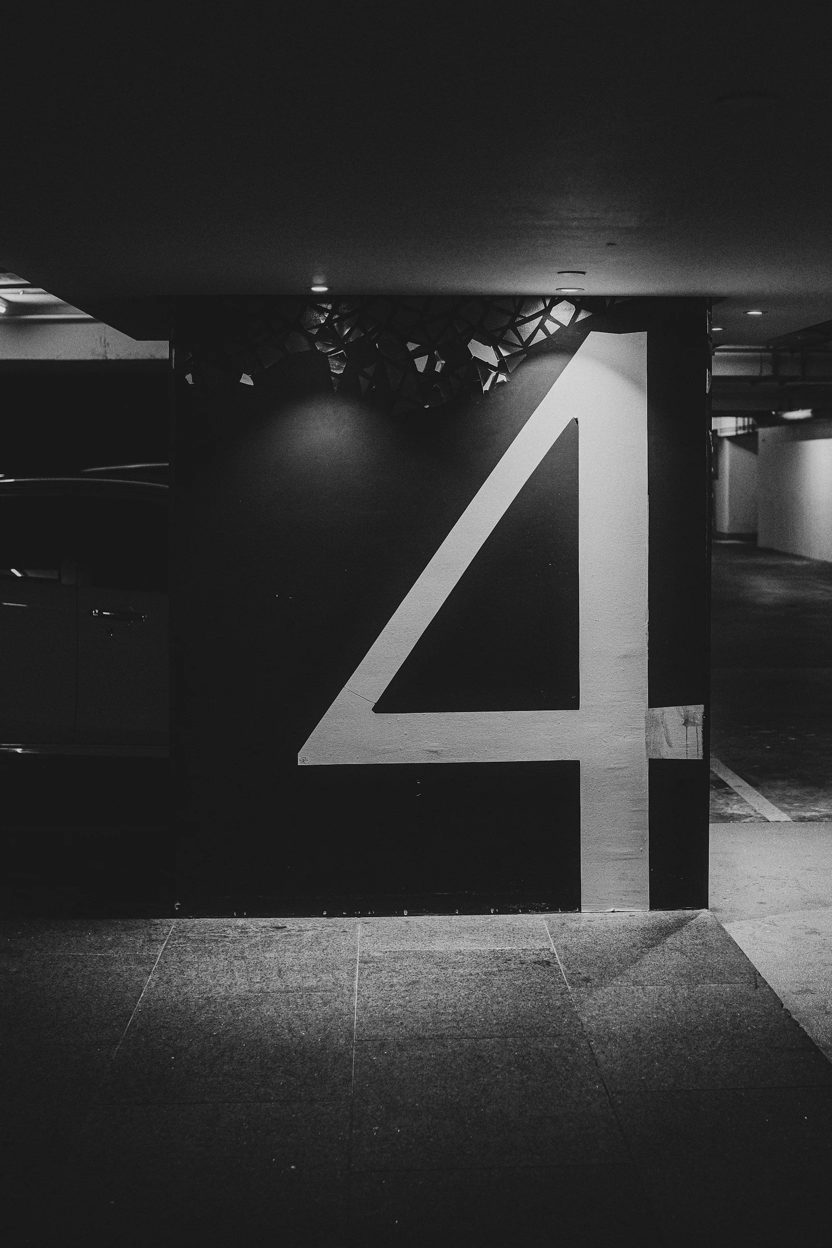 Black-and-white photograph of a parking garage wall with a large white number 4 painted on it.