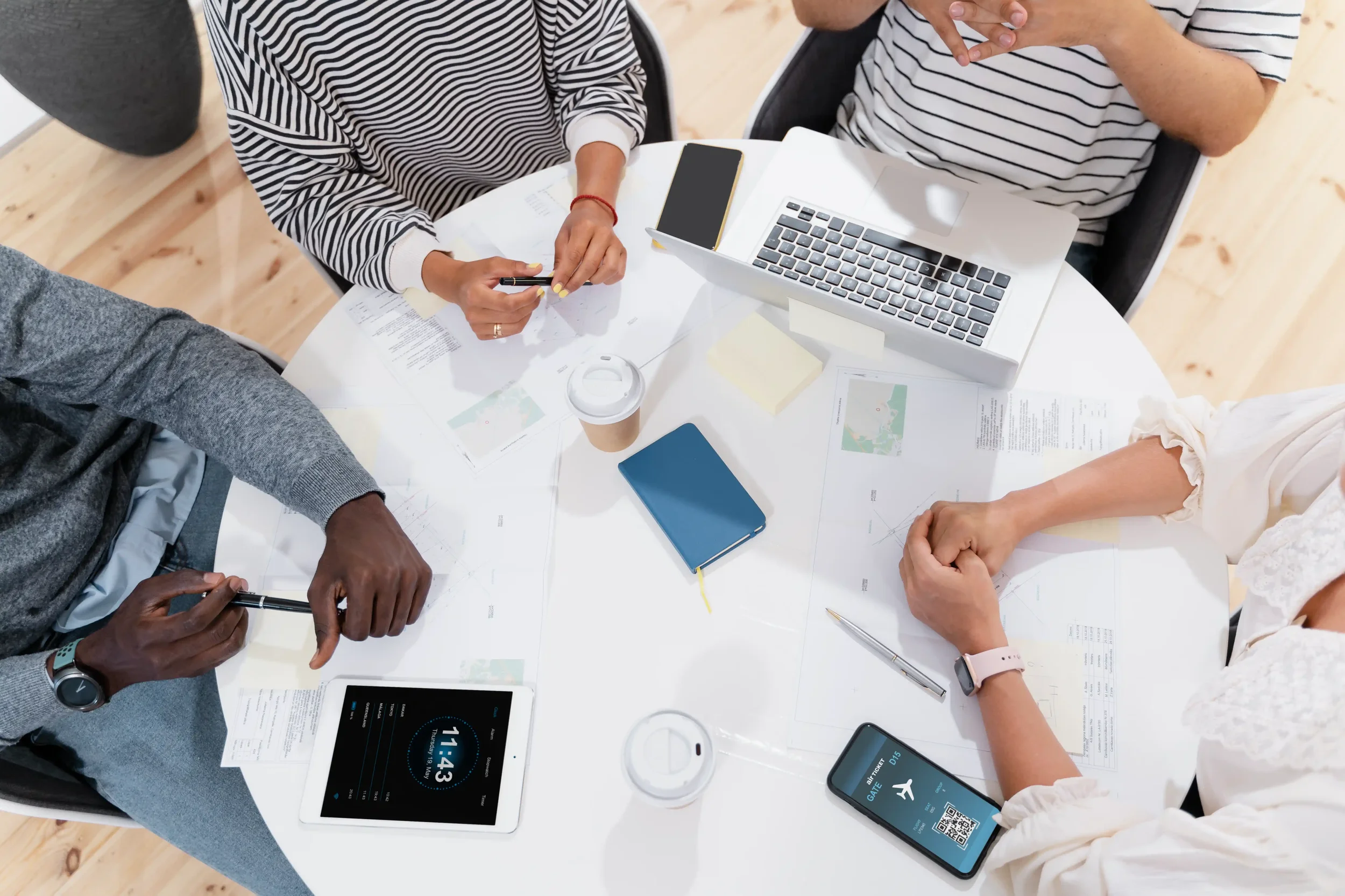 People sitting around a table with laptops, smartphones, and documents, engaged in a discussion or meeting.