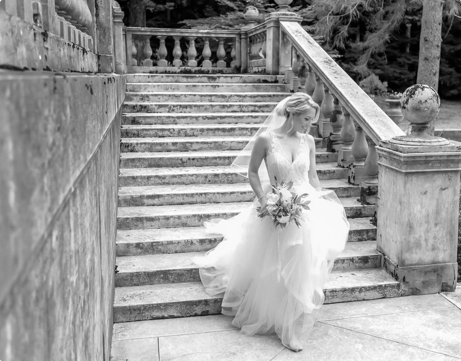 Black and white photo of a bride in a wedding dress walking barefoot downs the stairs