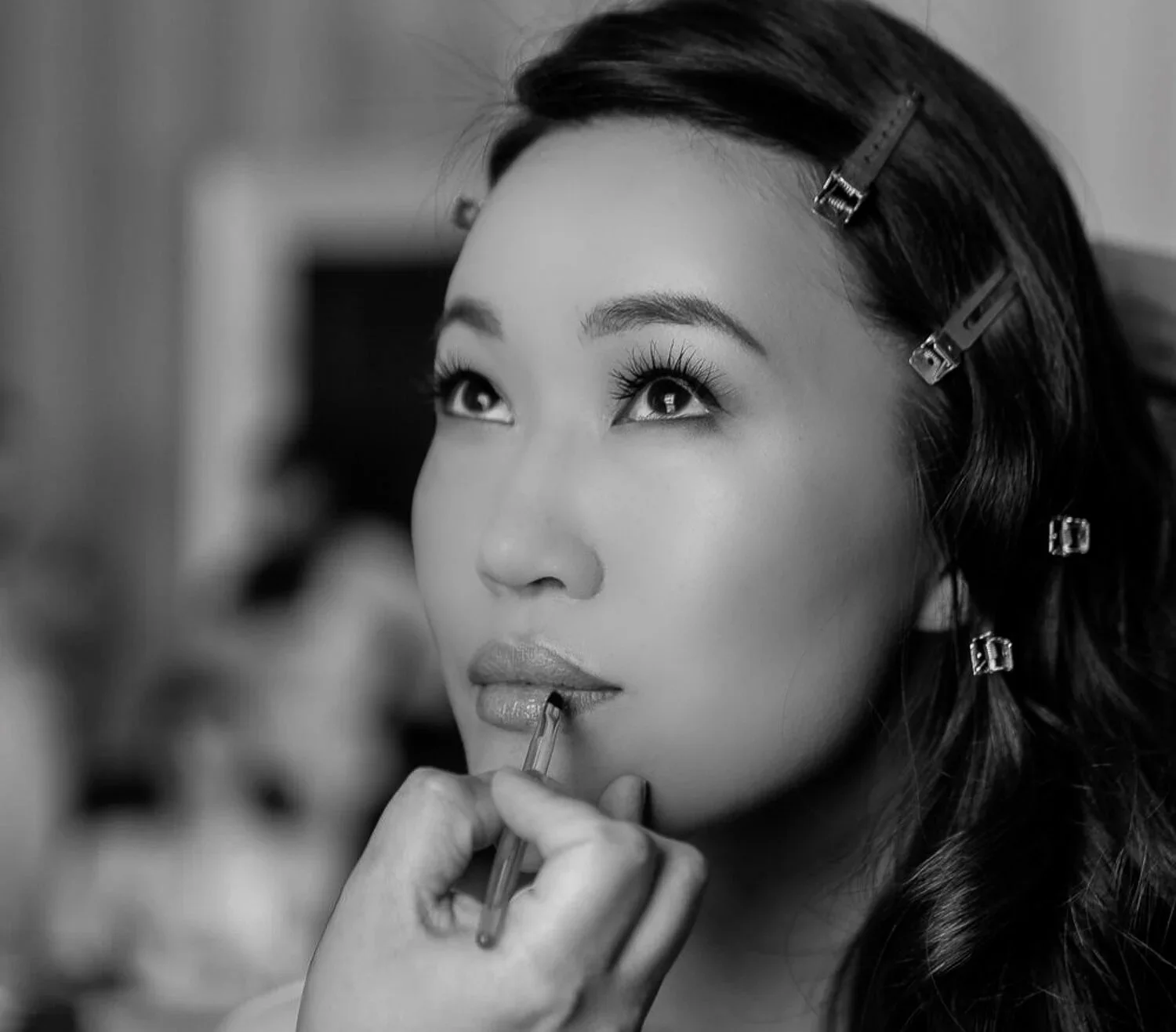 A woman with hair clips getting makeup applied to her lips.