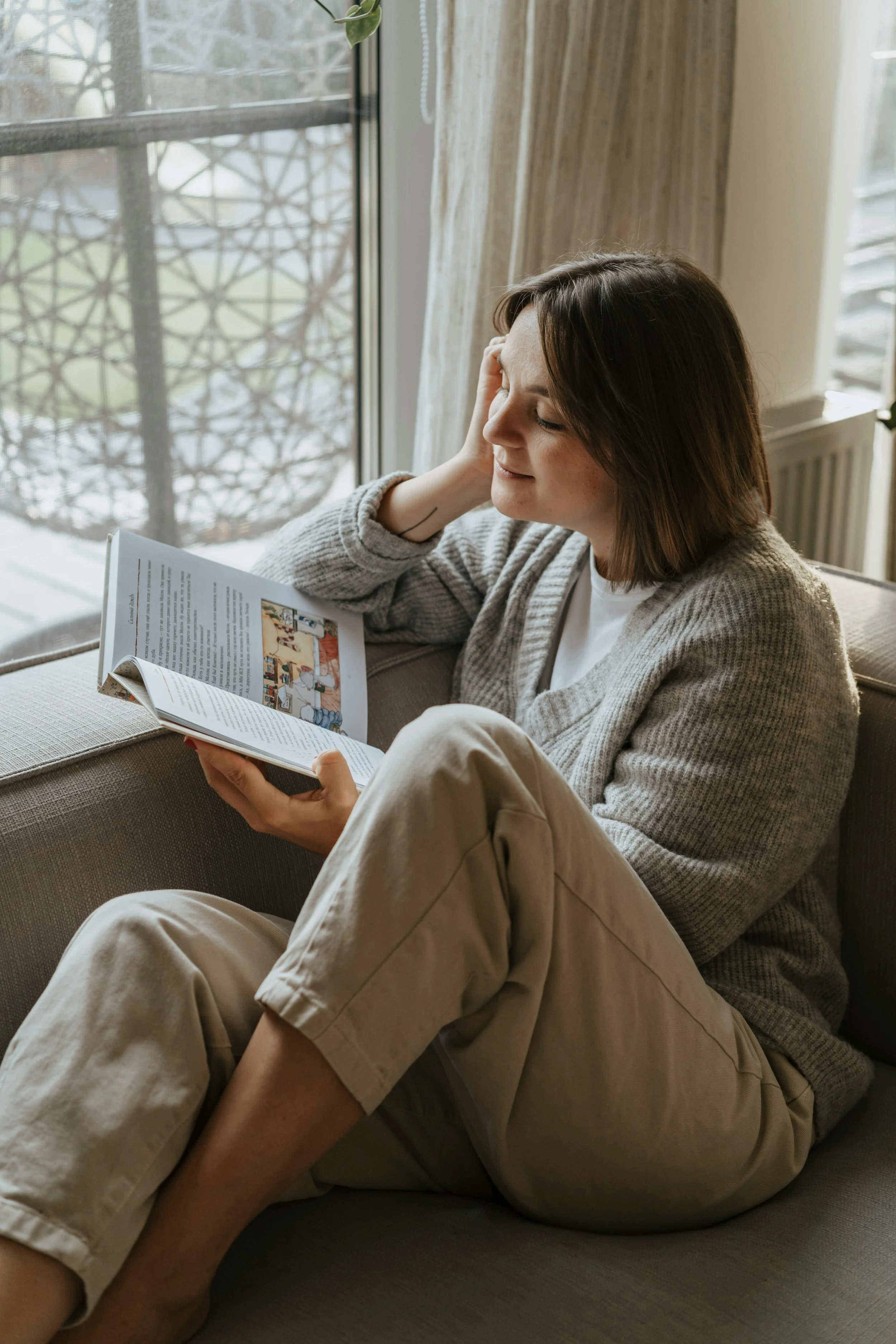 woman enjoying reading a book at a windowsill feeling relaxed.