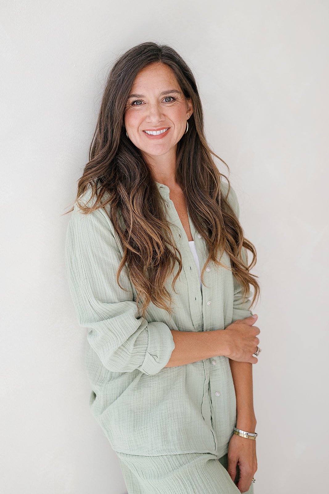 Jessica Ortiz, licensed therapist, owner of Catalyst Therapy & Consulting smiling leaning against white wall.