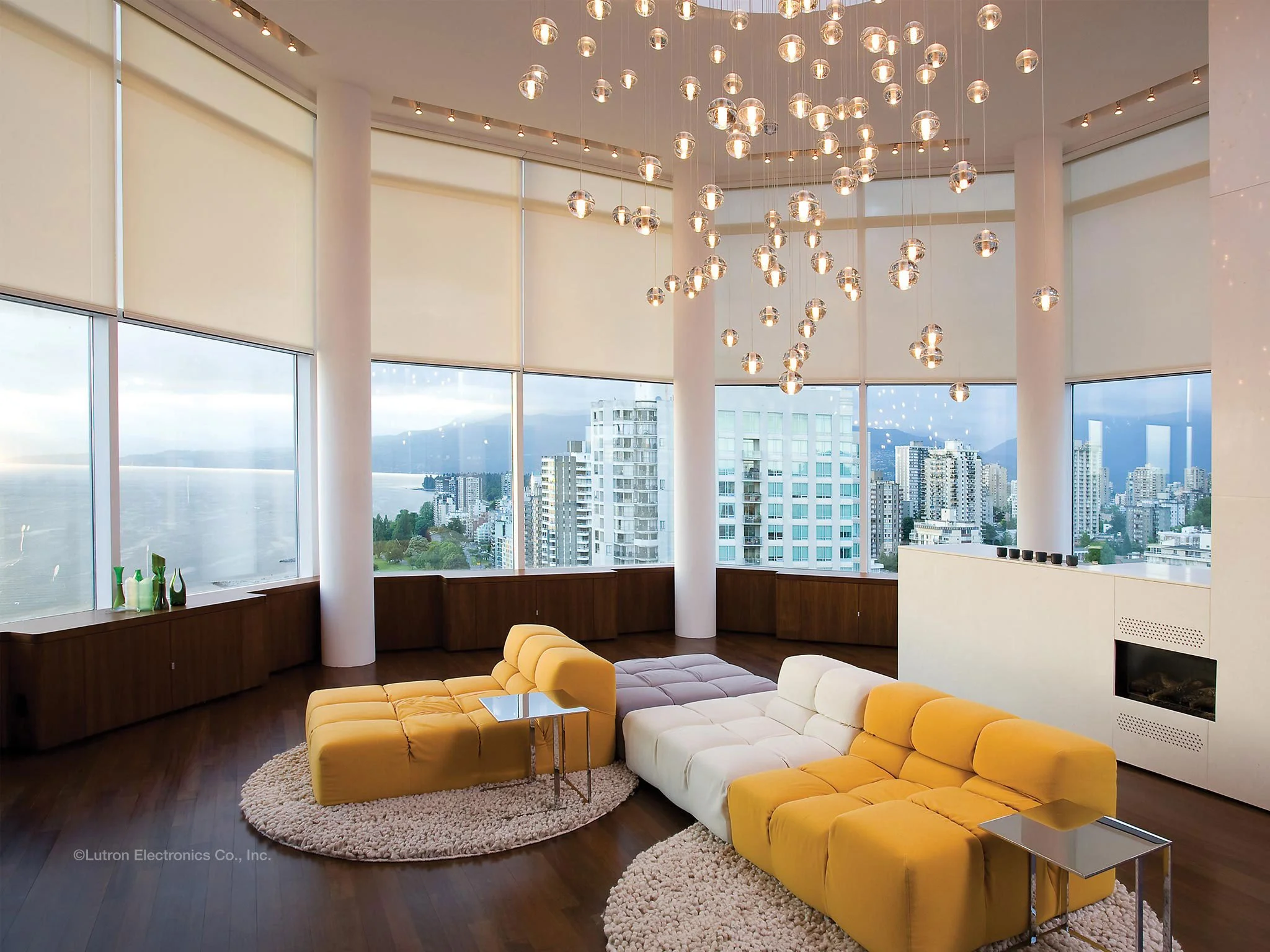 Modern, high-rise living room with large windows, cityscape view, contemporary yellow and white sectional sofa, glass side tables, textured rugs, and a decorative hanging light fixture.