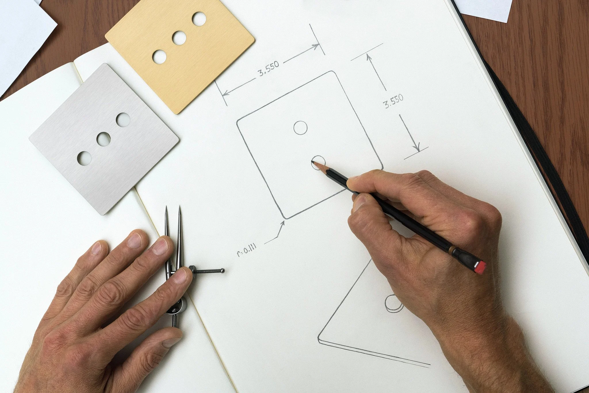 Person sketching technical drawing of a square automated lighting component with circular holes, measurements, and annotations on a white notebook page.