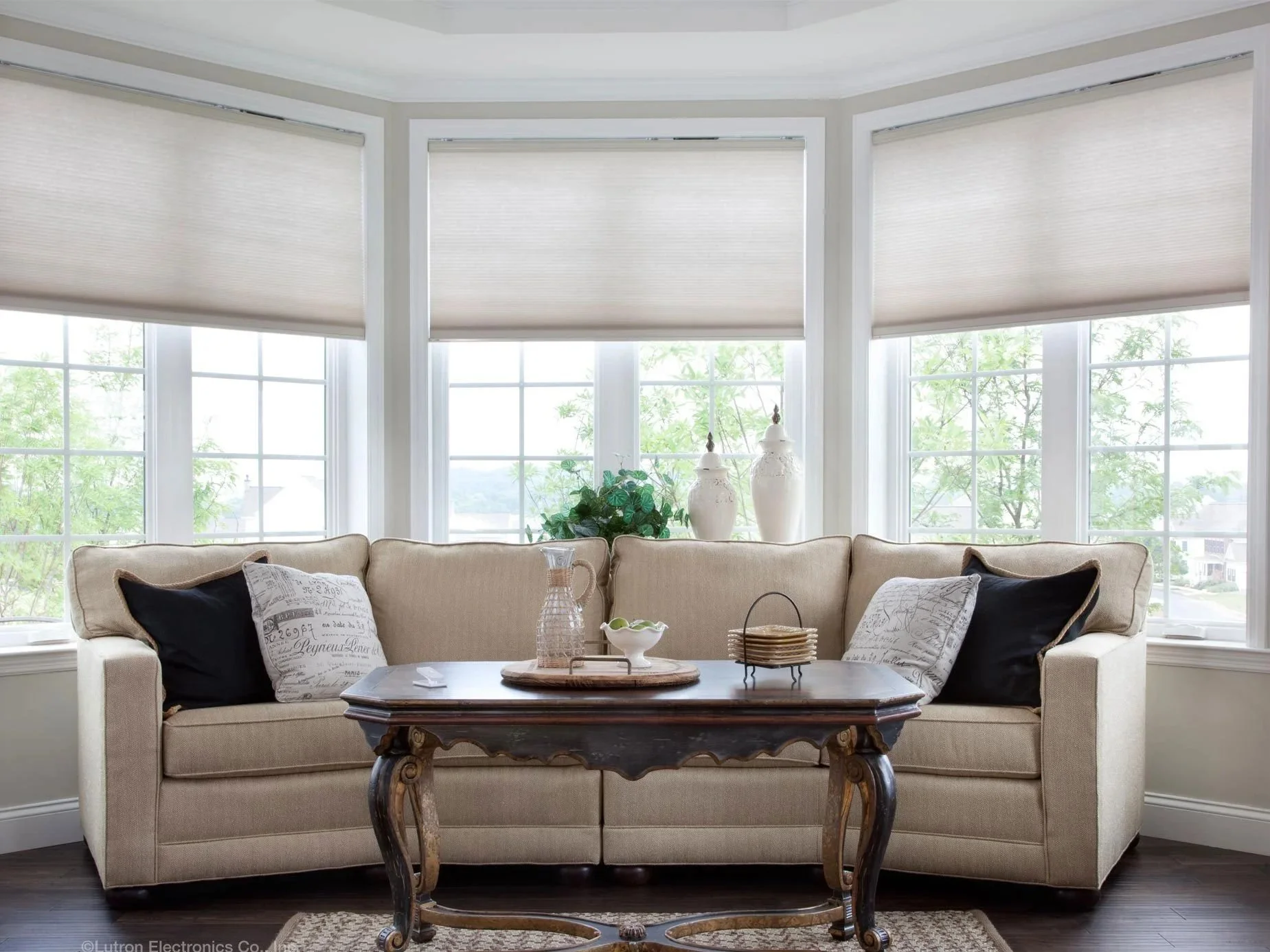 Bright living room with custom cellular window shades by Smart Shade Studio, featuring Clara Shades and Lutron light-filtering honeycomb shades on bay windows.