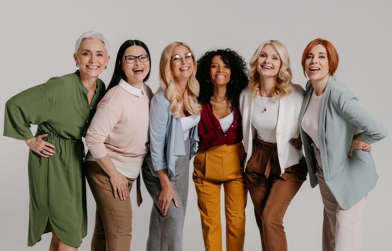 Six women standing together smiling against a plain white background.