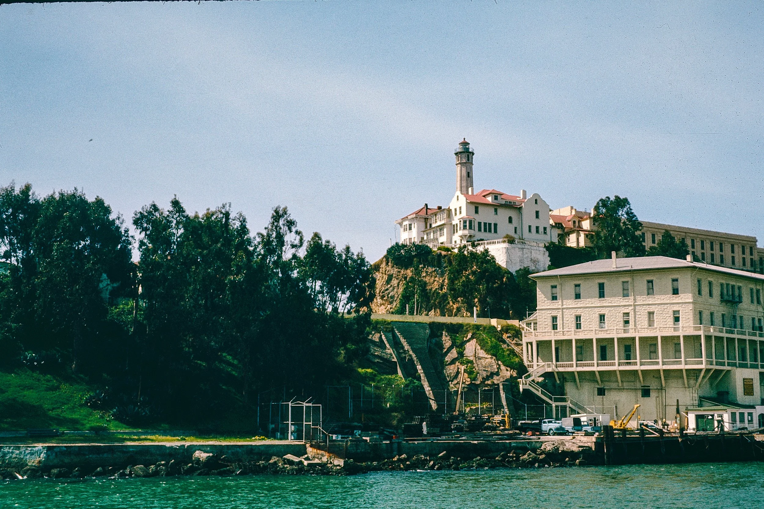 A large white building with a lighthouse on top, situated on a hill, overlooking the water and surrounded by trees.