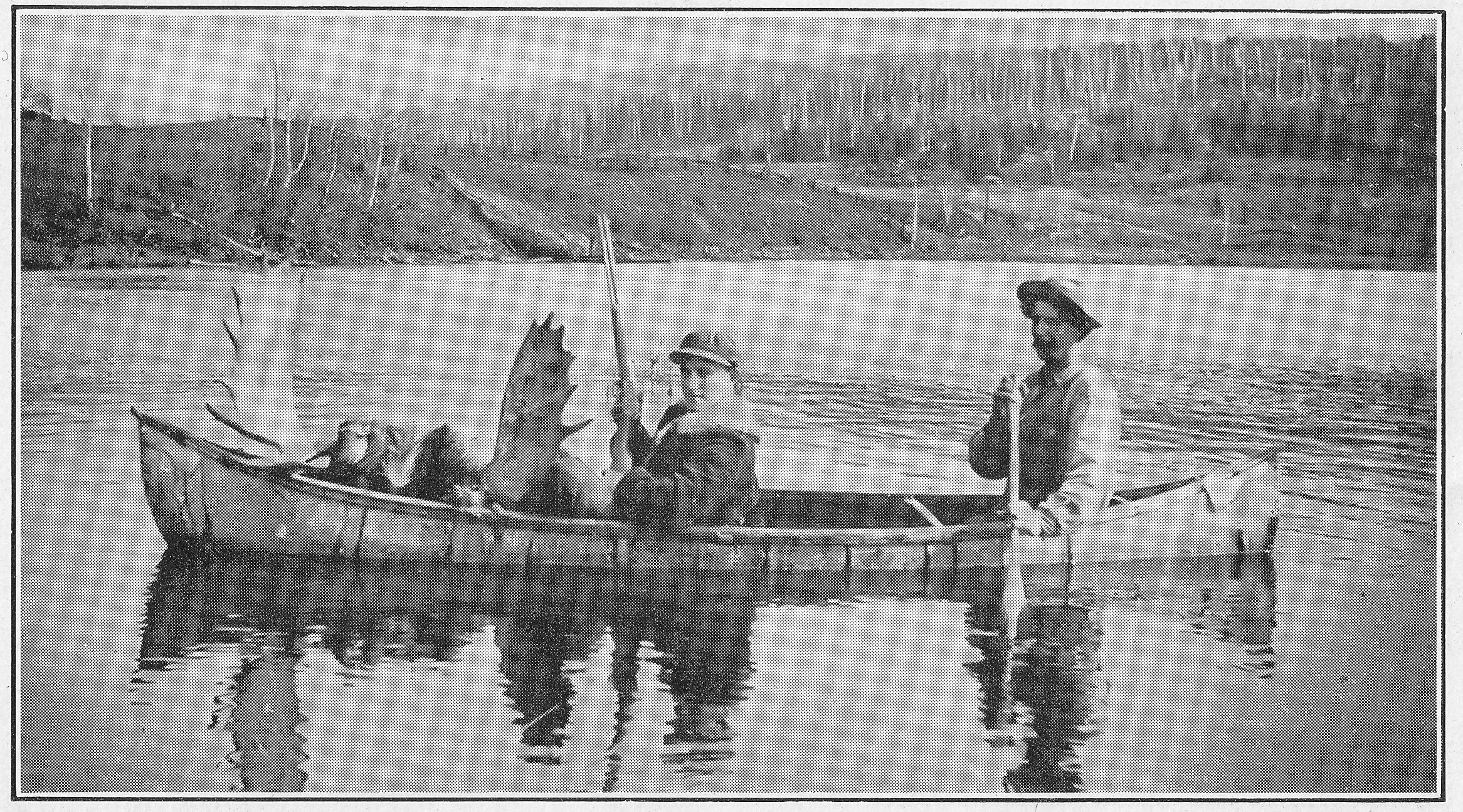 Two people in a small boat on a lake, one holding a paddle and the other sitting near the boat's bow, with a hilly landscape and trees in the background.