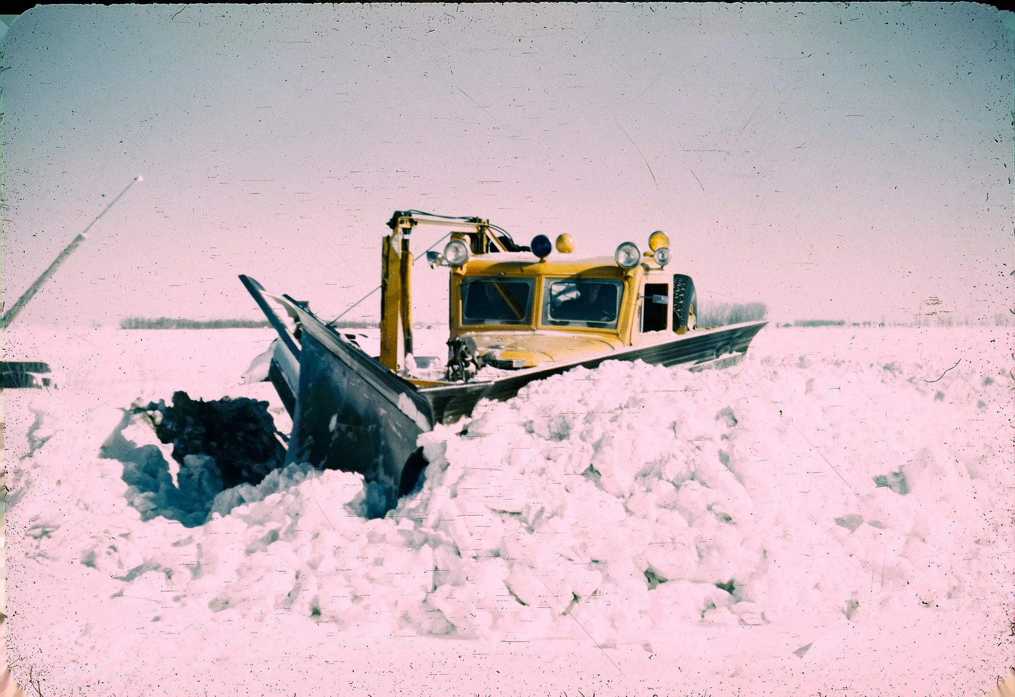 A yellow snowplow clearing snow in a snowy landscape under a cloudy sky.