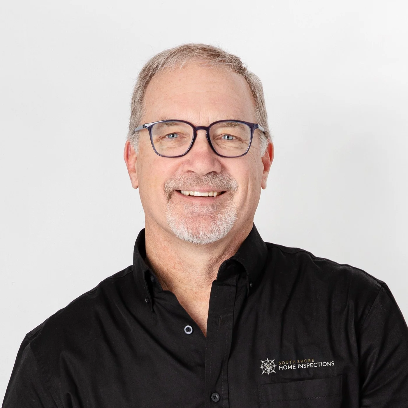 A middle-aged man with glasses, gray hair, and a beard smiling, wearing a black shirt with a logo for South Shore Home Inspections.