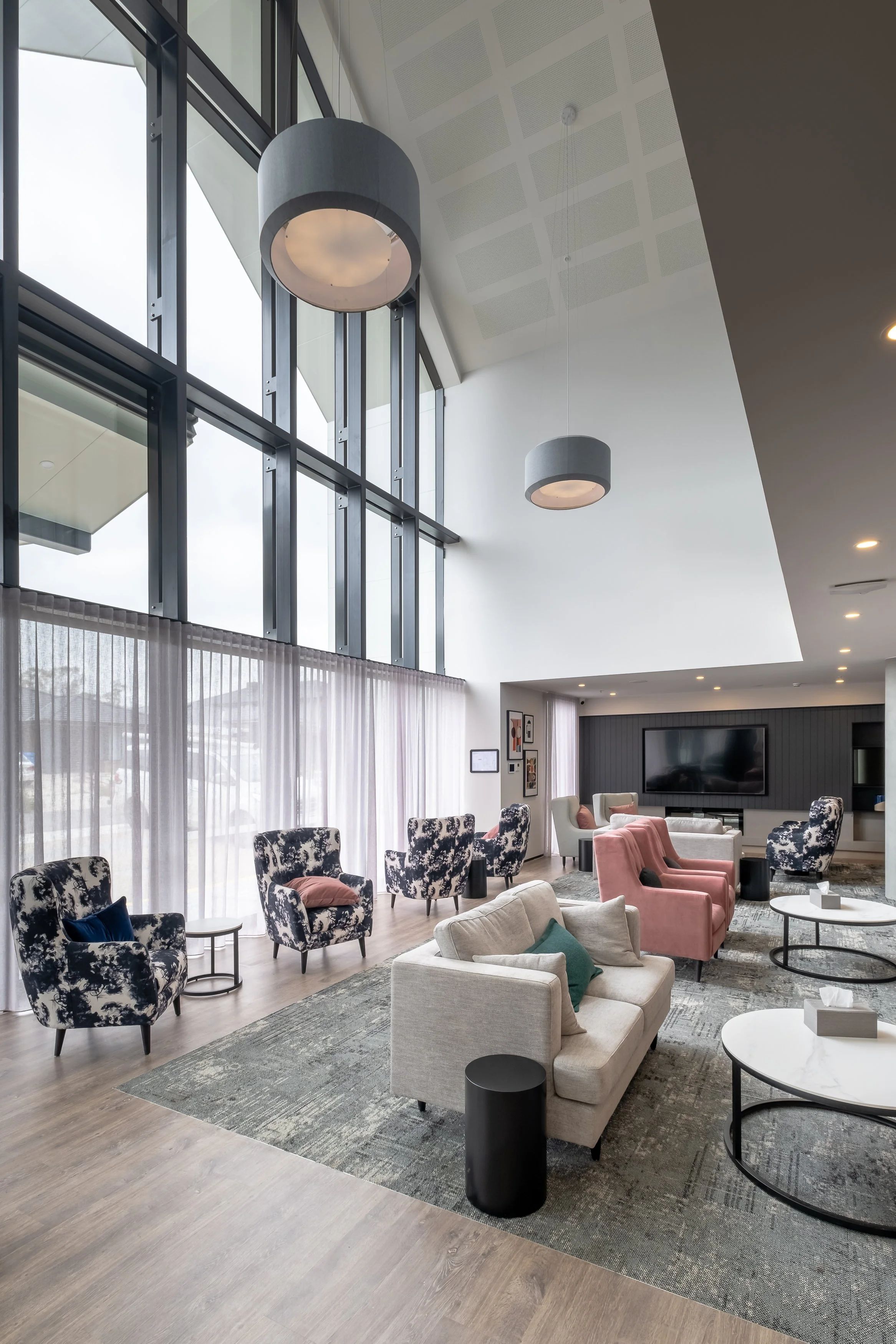 Modern lobby with large windows, hanging lights, and a variety of armchairs and sofas arranged around circular tables.