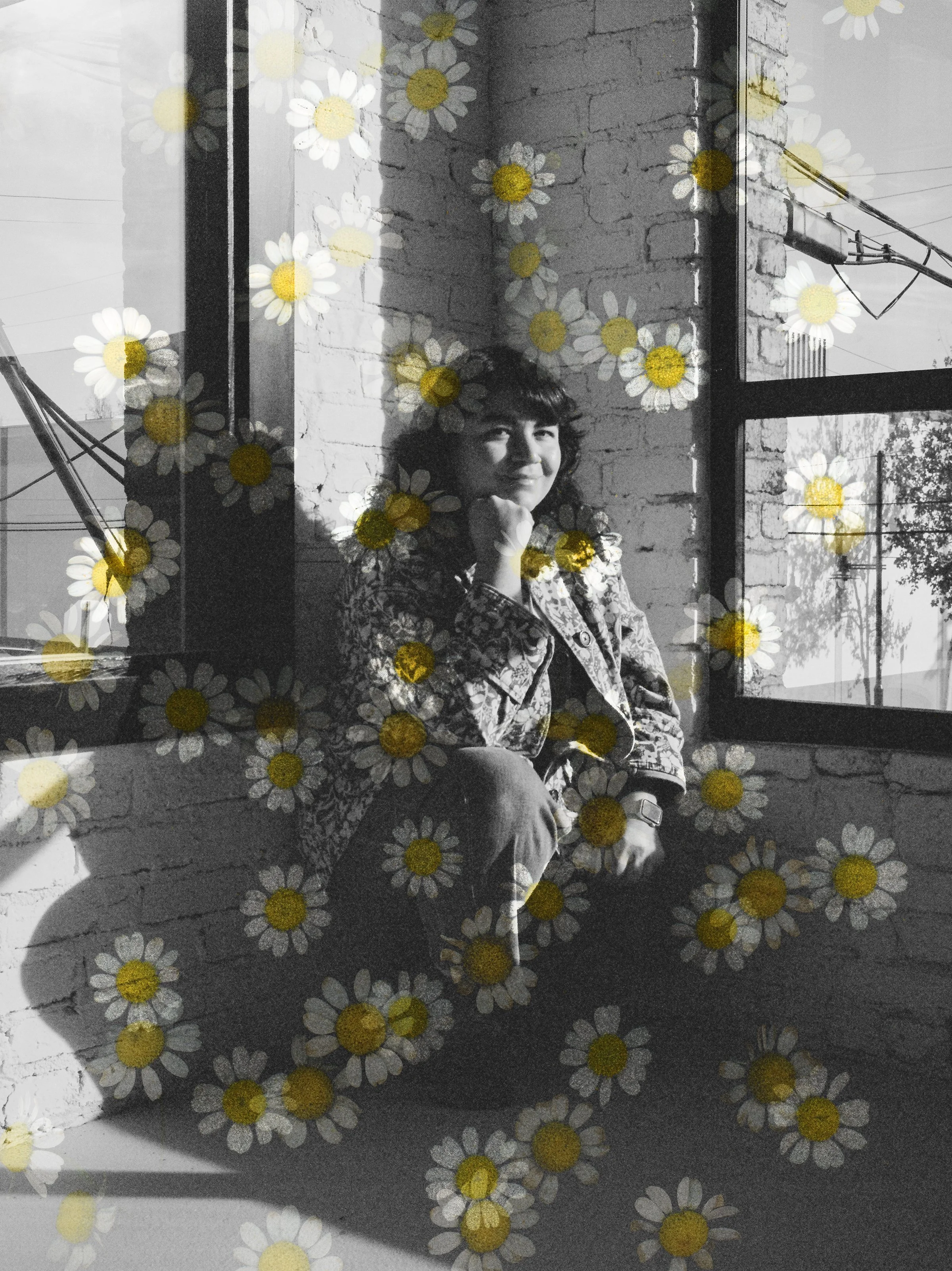 black and white photo of a woman in her early 40s squatting in a corner between windows and smiling with an overlay of chamomile flowers over the image
