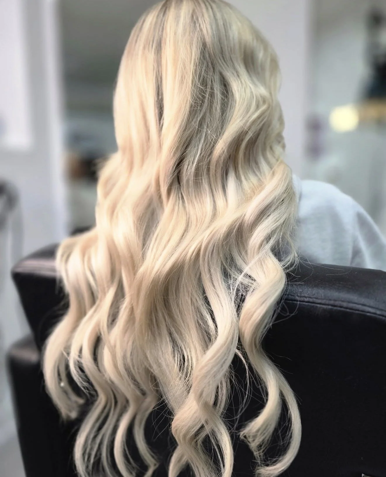 Blonde hair with loose waves on a person sitting in a chair in a salon setting.