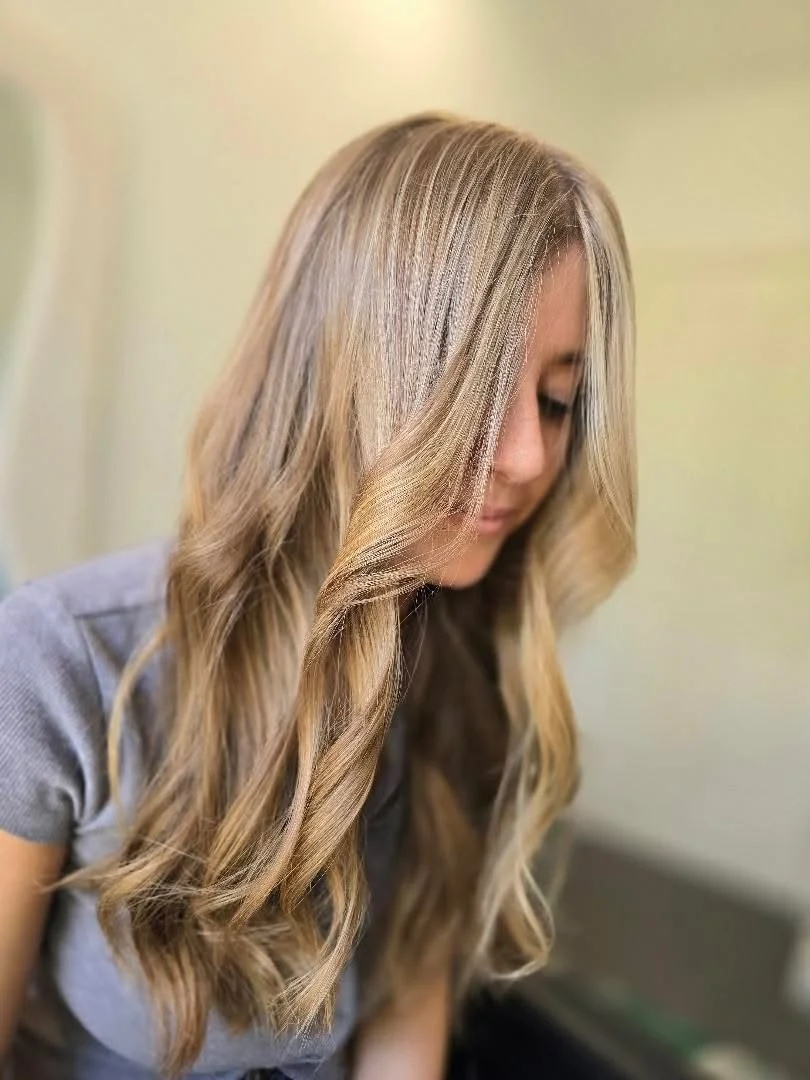 A woman with long, blonde, wavy hair looking down.