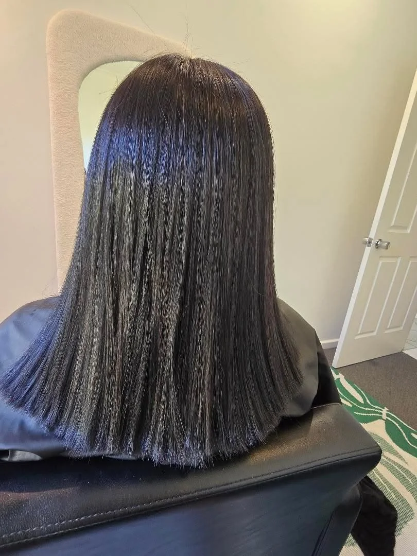 Back view of a woman with straight, shiny, black shoulder-length hair sitting on a black salon chair.