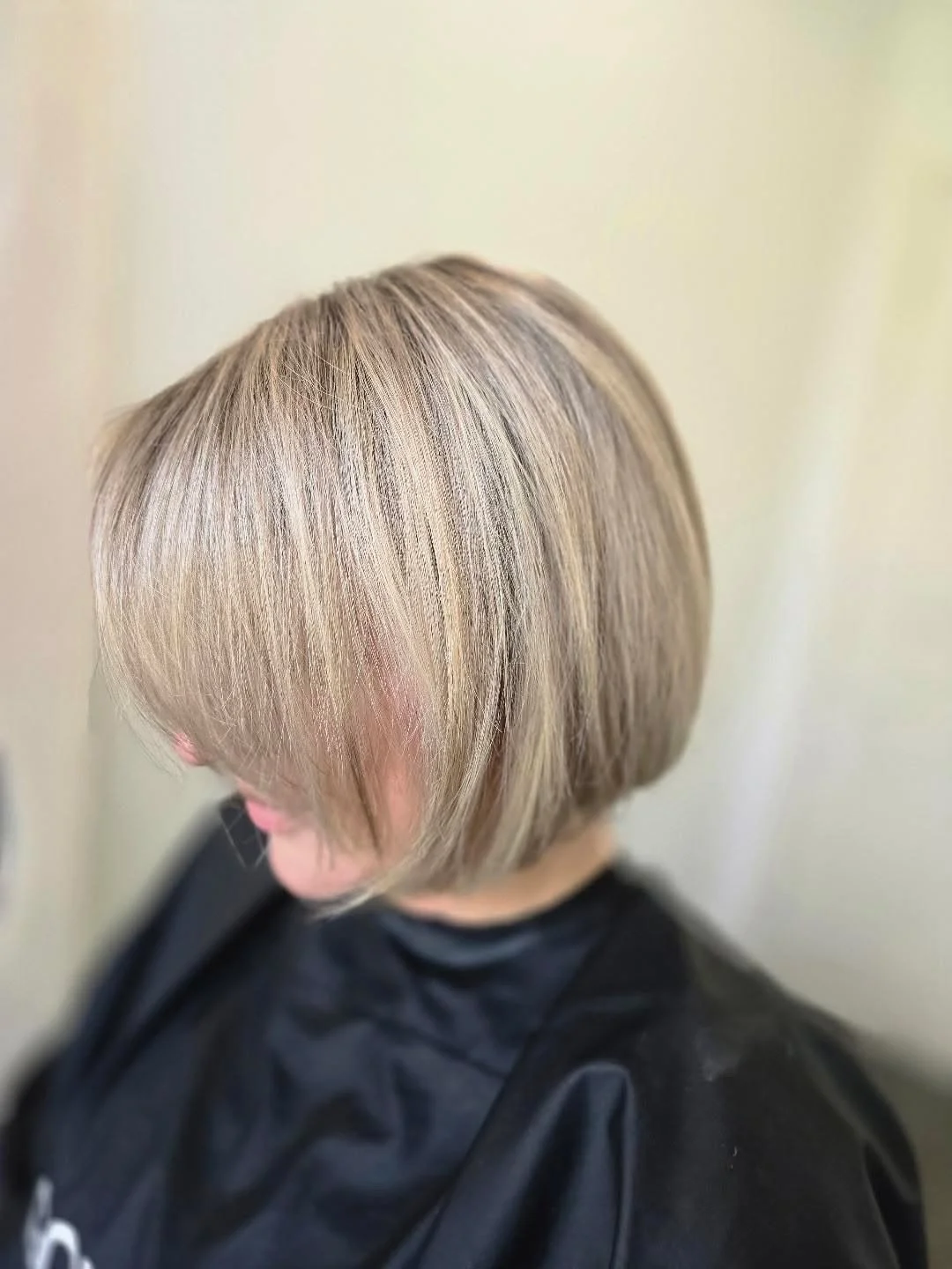 Close-up of a person with a short, layered blonde haircut, wearing a black cape at a salon.