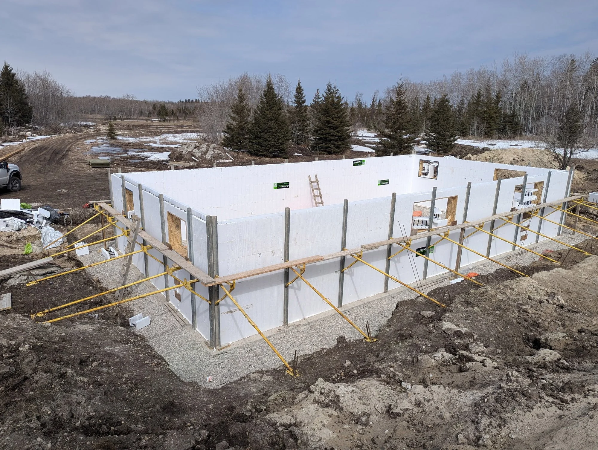 Construction site with ICF Basement walls in progress, surrounded by dirt and construction materials, with a rural landscape and trees in the background.