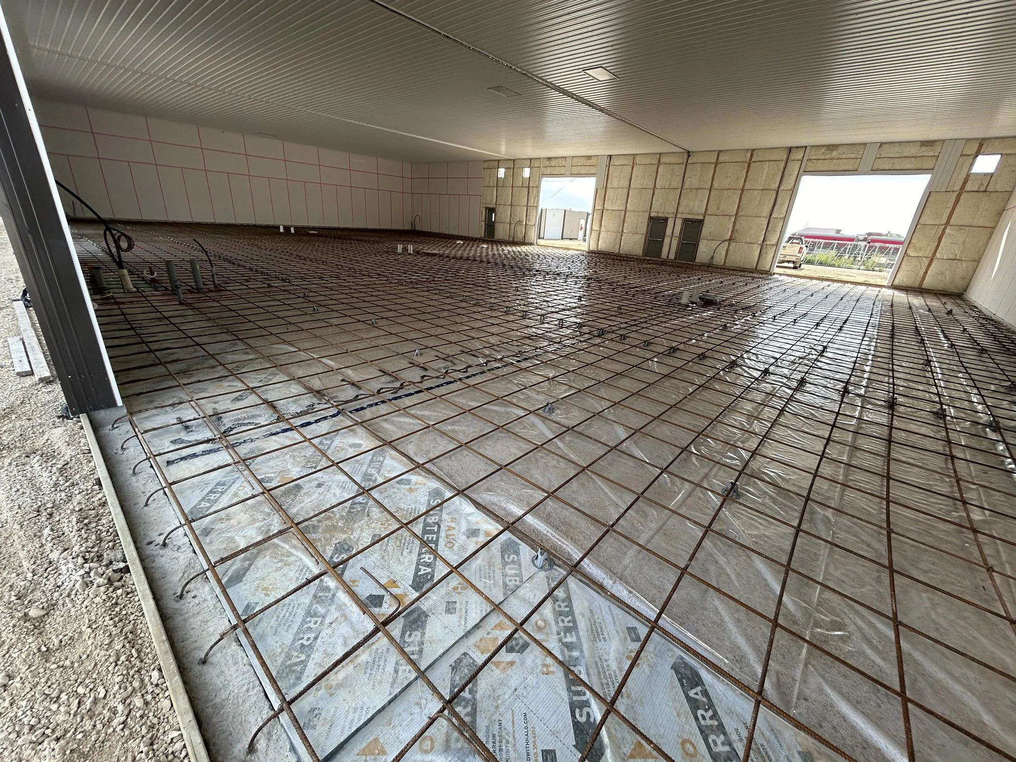 Building interior with exposed concrete walls and metal rebar grid on the floor, indicating construction or renovation ongoing.
