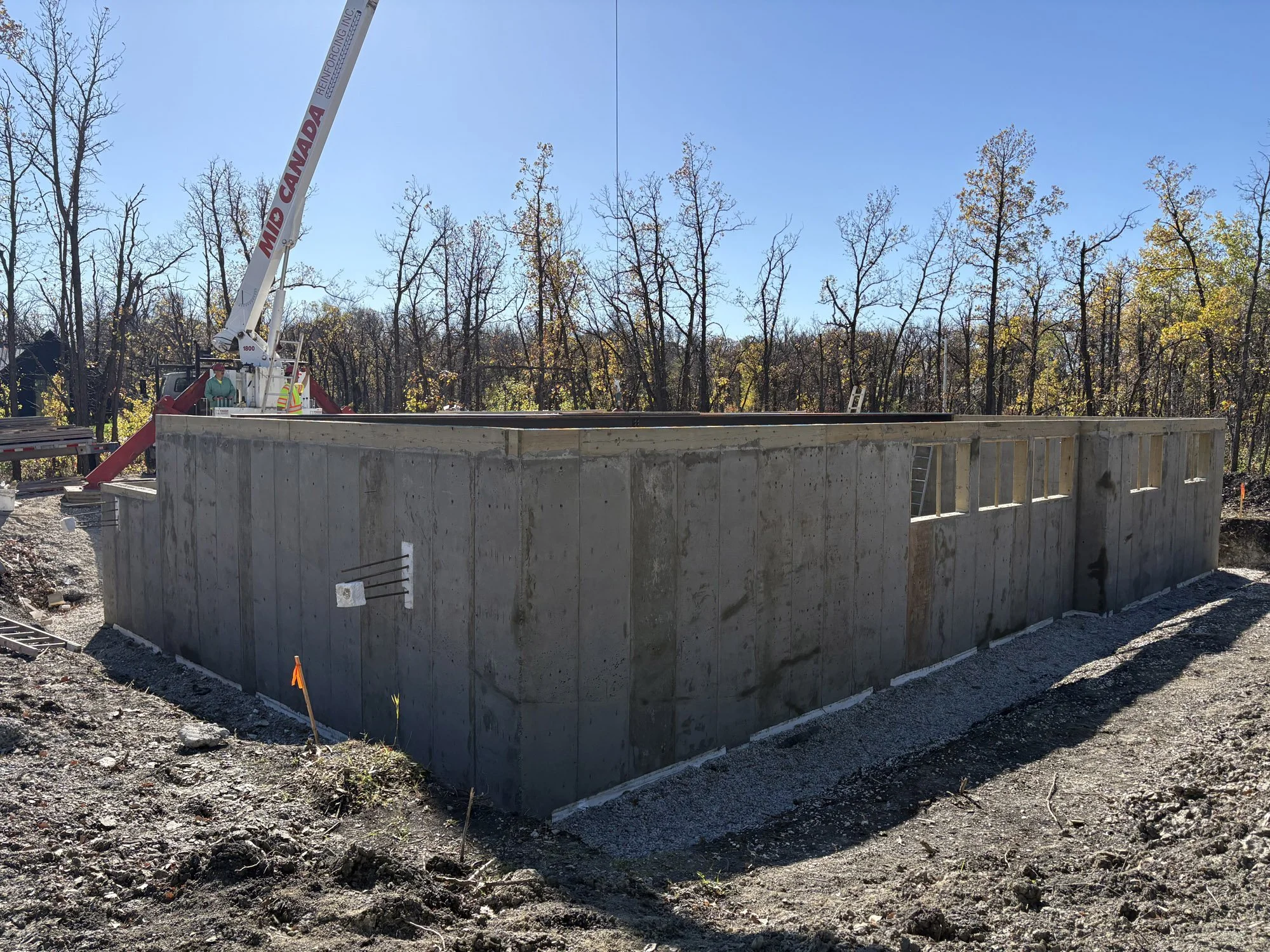 Concrete foundation of a building under construction with a crane in the background, surrounded by trees and clear sky.
