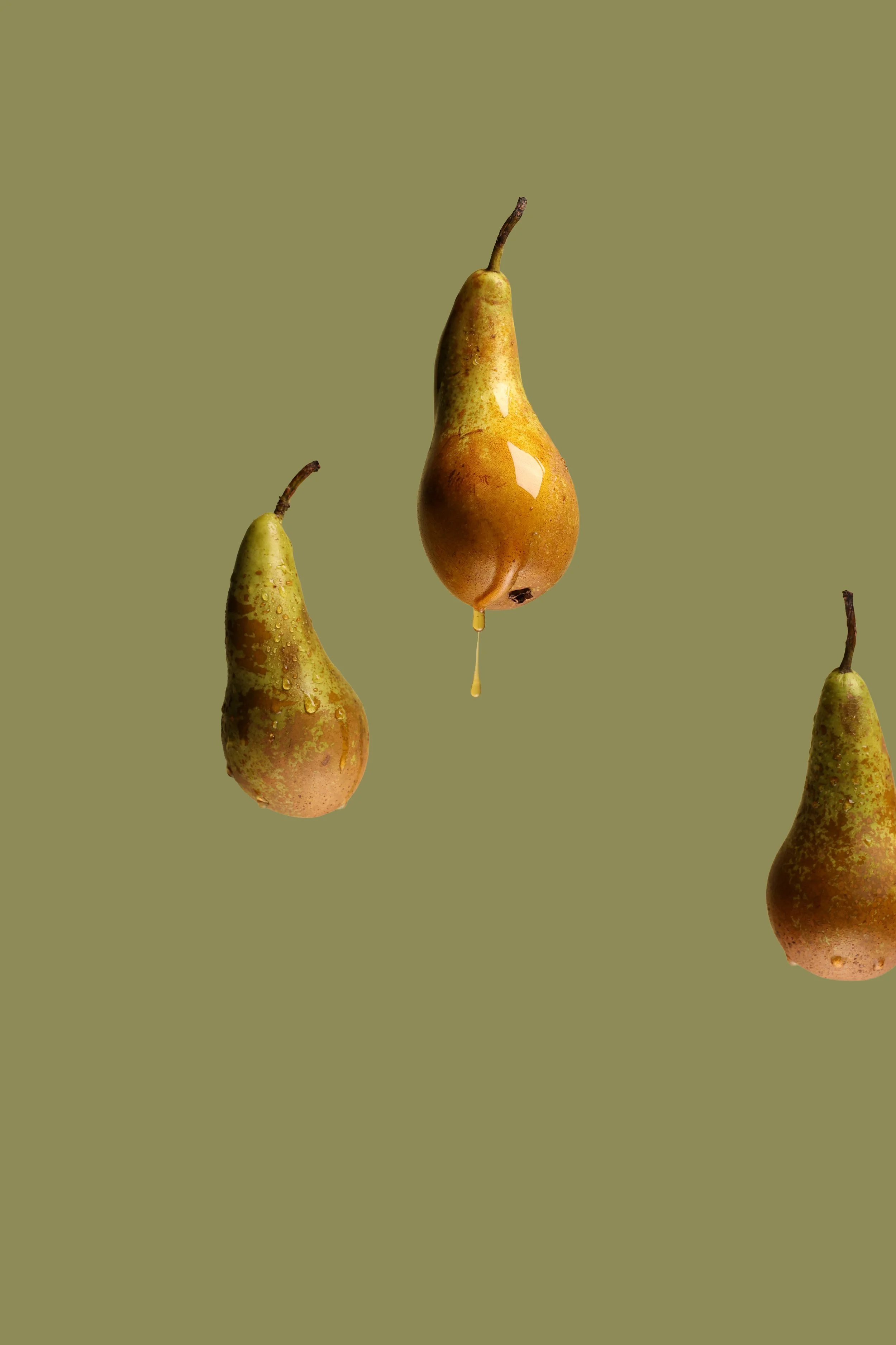 Three pears, one with spilled juice dripping from it, suspended against a muted olive green background.