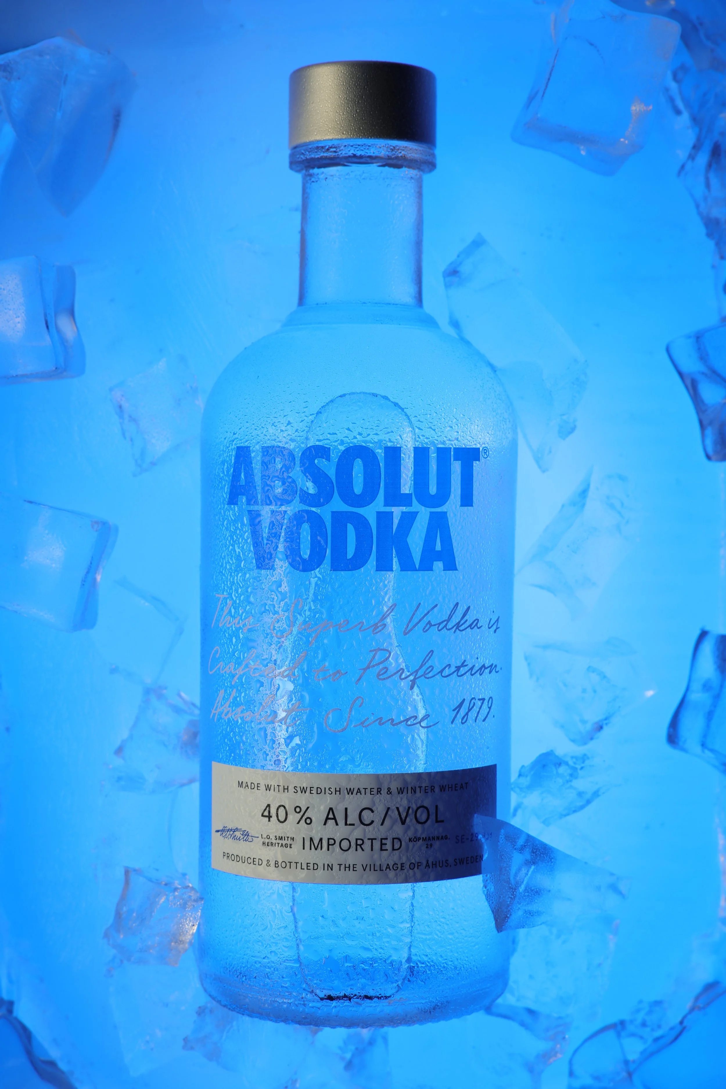 A bottle of Absolut Vodka surrounded by ice cubes under blue lighting.