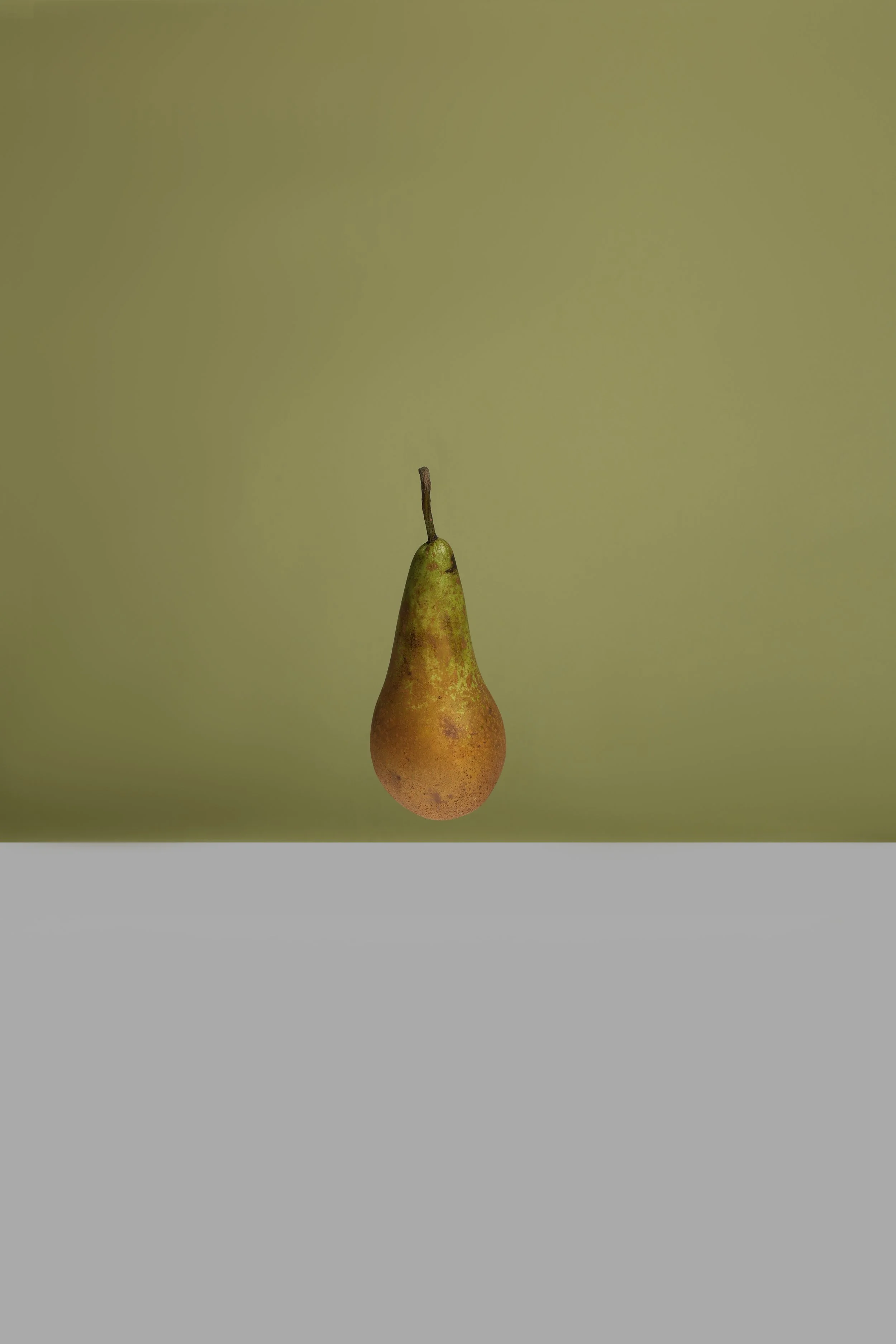 A pear hanging upside down against a plain, muted green background.