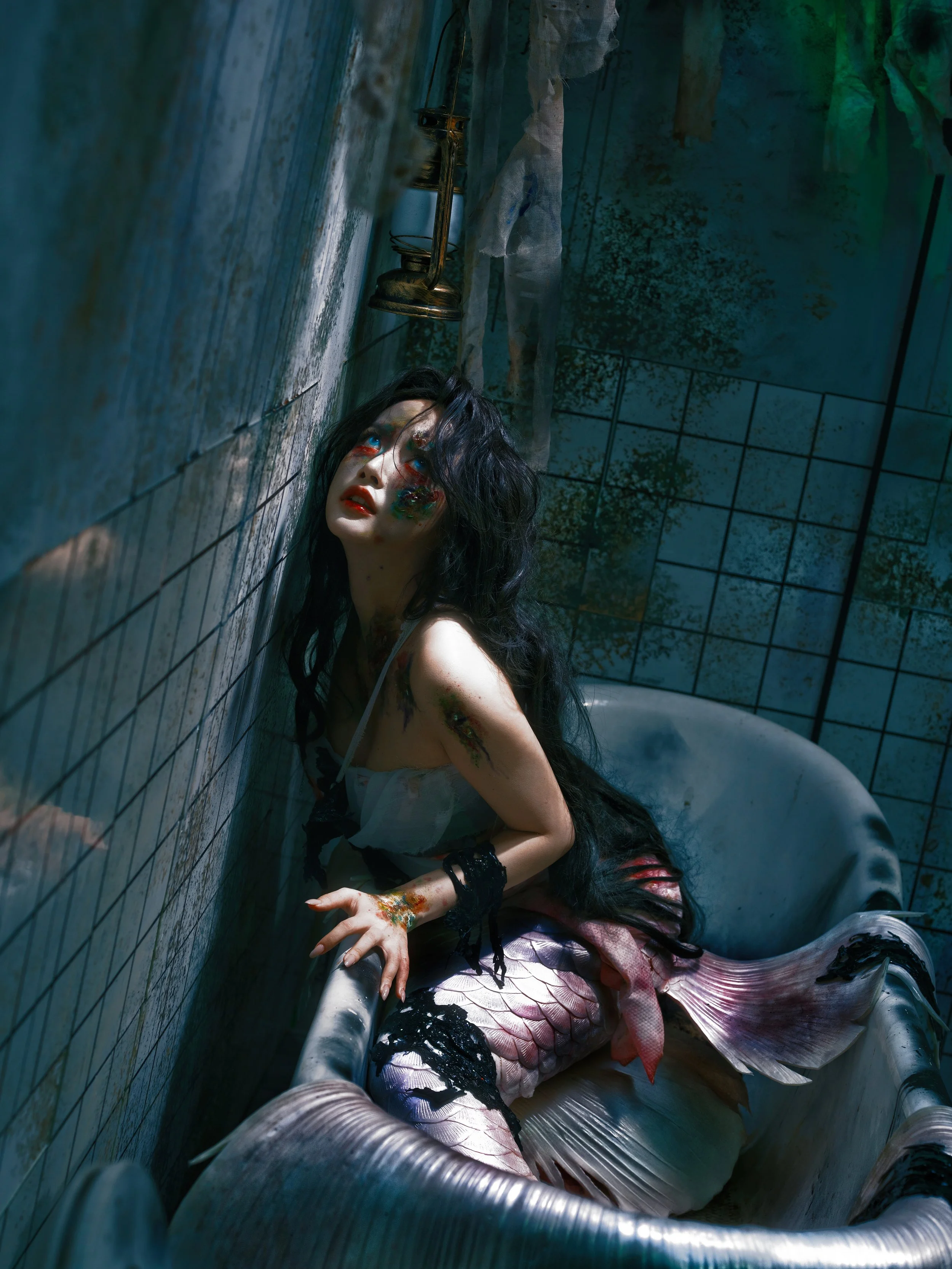 A person with a mermaid tail and dark hair sitting in an old bathtub in a dimly lit, dirty bathroom with peeling tiles and stained walls.