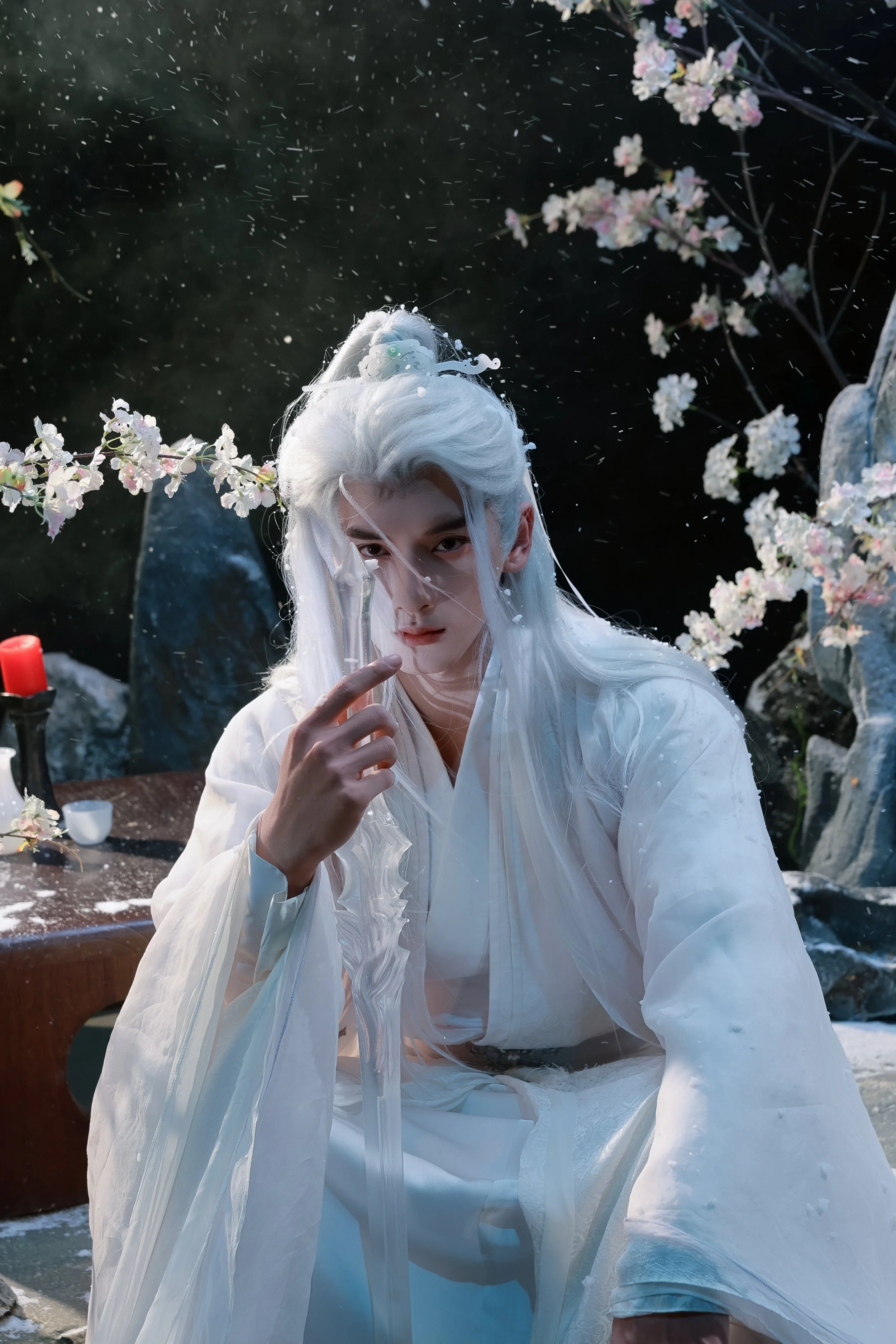 Person with long white hair dressed in traditional white clothing, surrounded by cherry blossoms, with a contemplative expression, and holding a translucent sword or staff, in a natural outdoor setting.