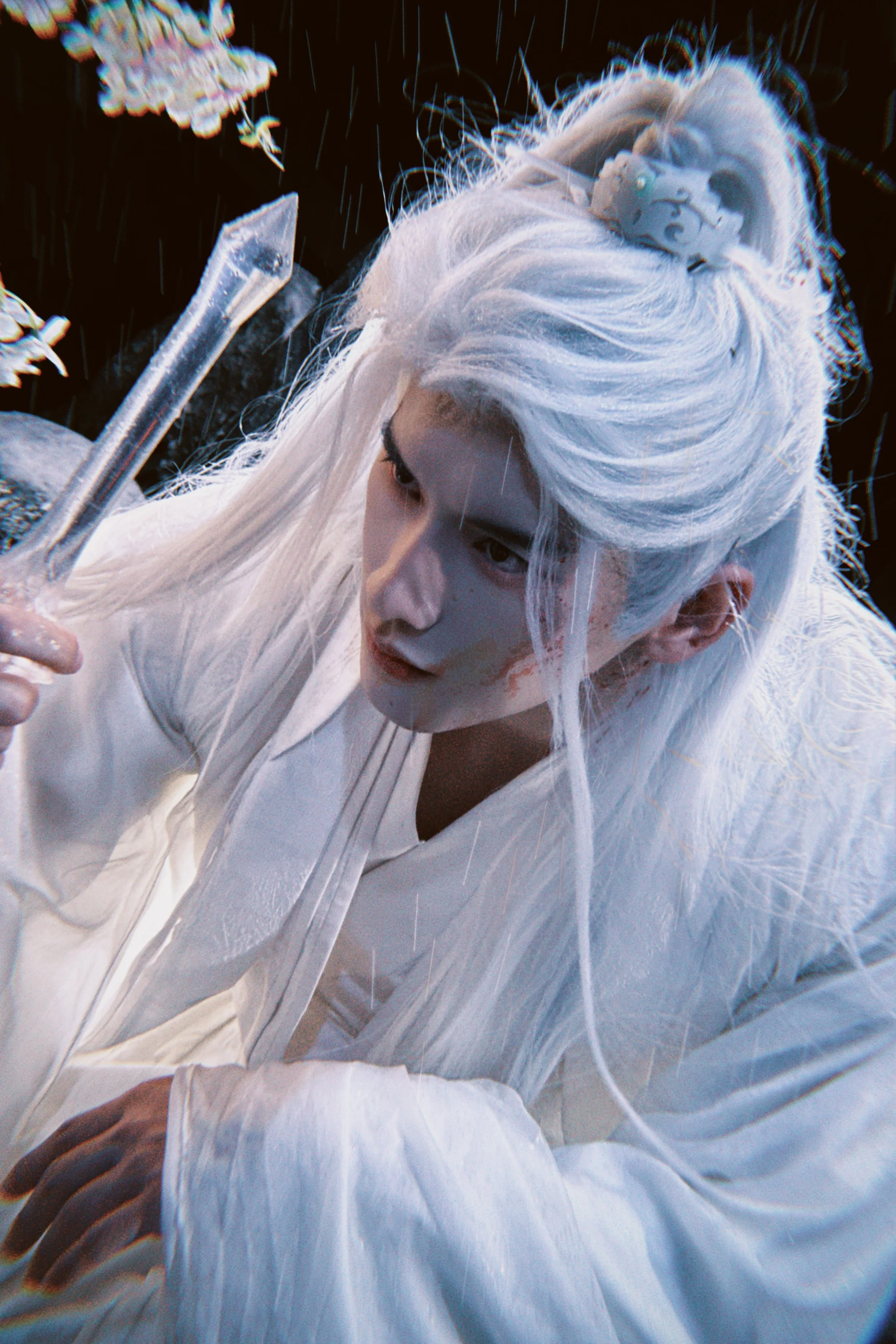 A person with long, white hair dressed in white holding a test tube.