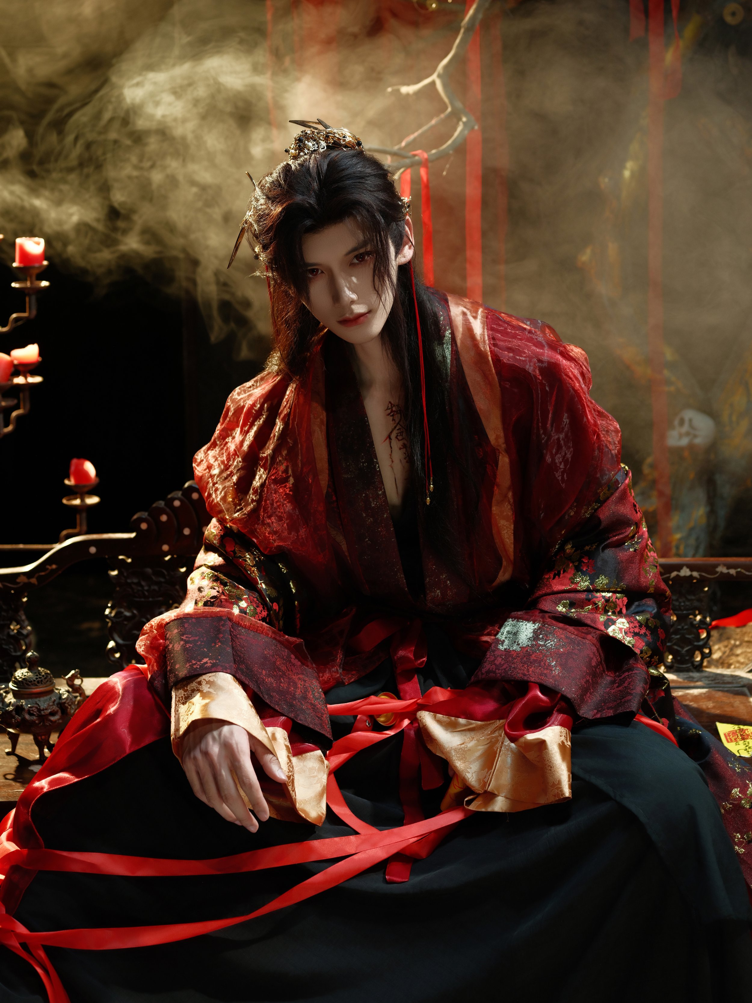 A person dressed in traditional Asian, possibly Chinese, attire with dark hair and intricate accessories, sitting on a decorated wooden bench, with dim lighting and red accents around.