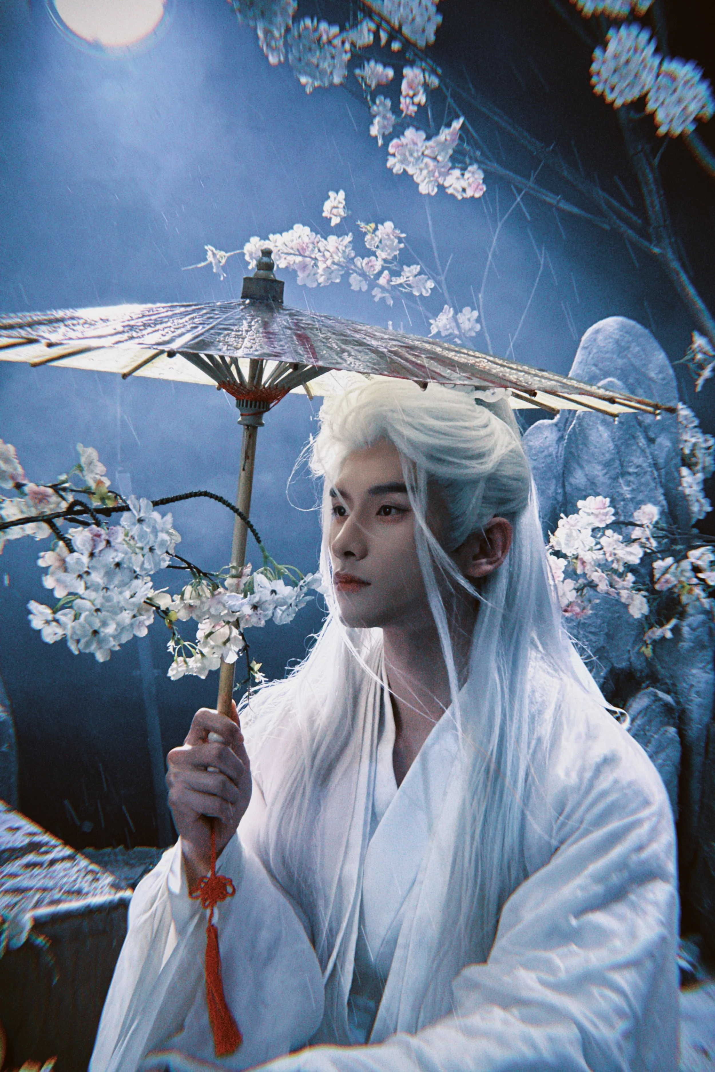 A person dressed as a traditional or fantasy character with long white hair, holding a paper umbrella decorated with cherry blossoms, in a setting with cherry blossoms and a full moon in the night sky.