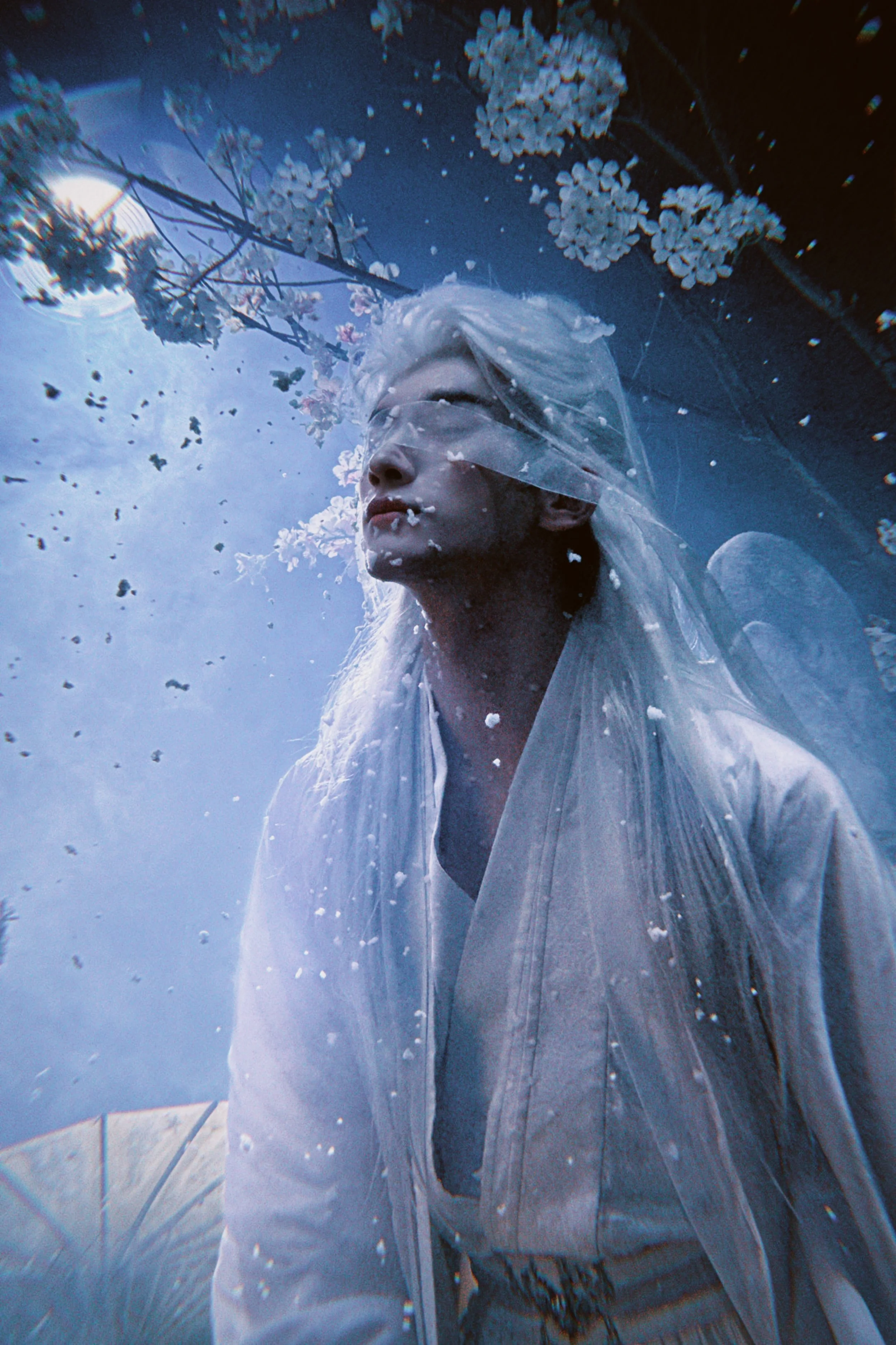 A person with platinum blonde hair and a veil, wearing a white outfit, standing outdoors at night with moonlight, surrounded by blooming white flowers and sparkles in the air.