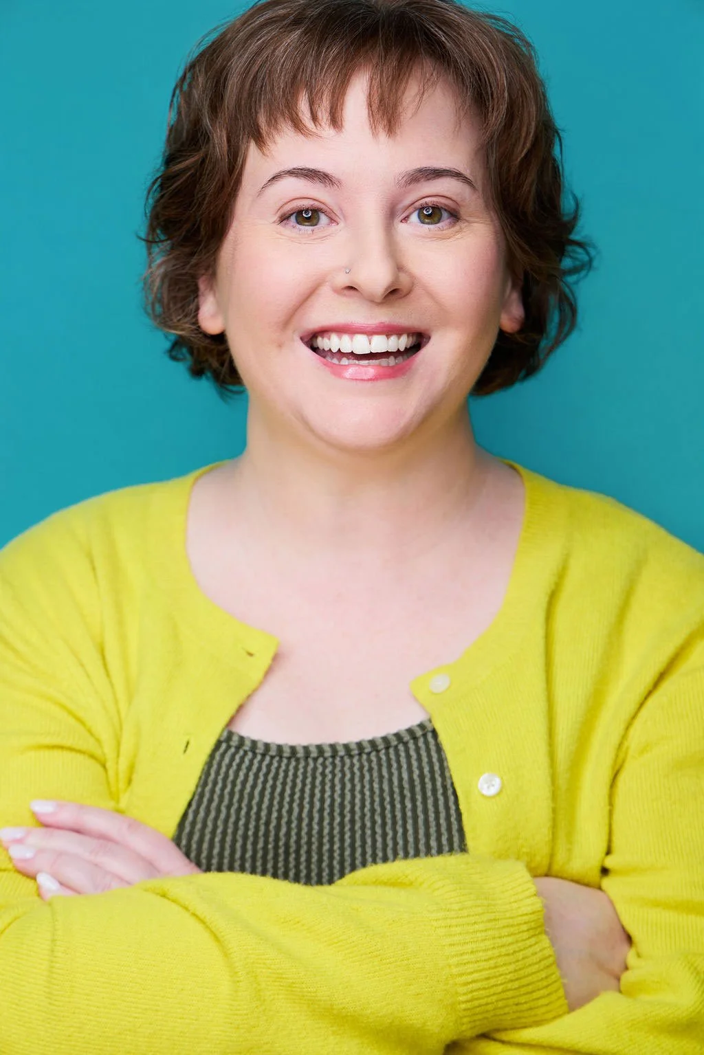 Sue Gauthier has her brown hair down, an open-mouthed smile, looking at the camera. Wearing a bright yellow cardigan and a white undershirt, showering her range as an actress/writer.