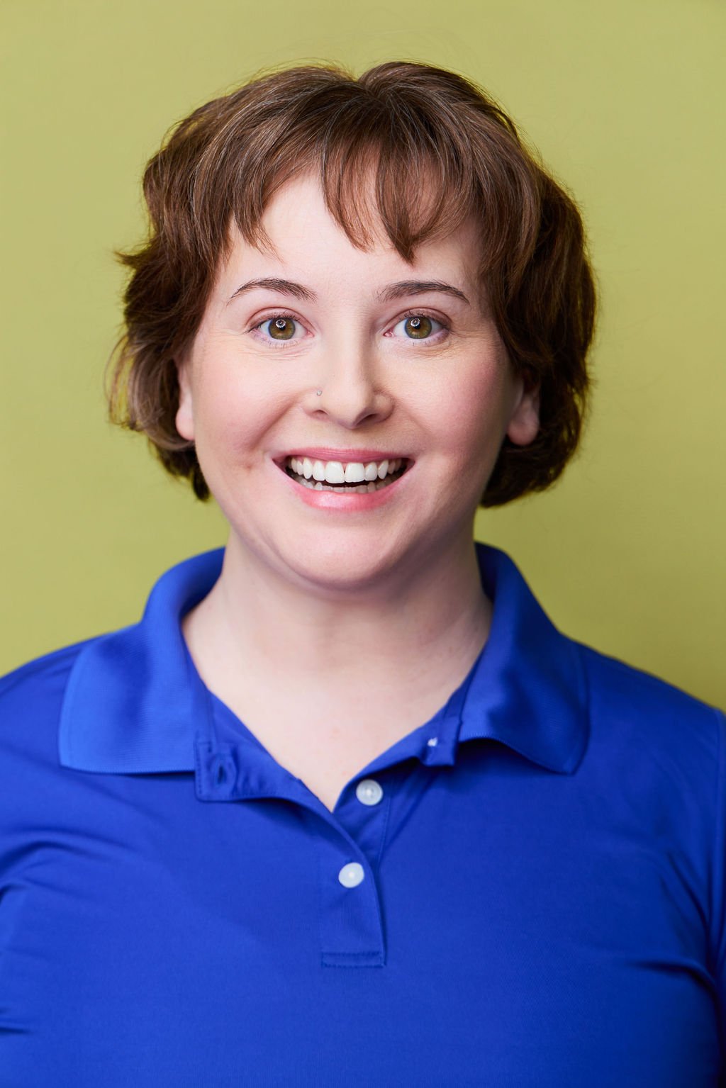 Sue Gauthier has her brown hair down, an open-mouthed smile, looking at the camera. Wearing a blue polo shirt, showing her range as an actress/writer.