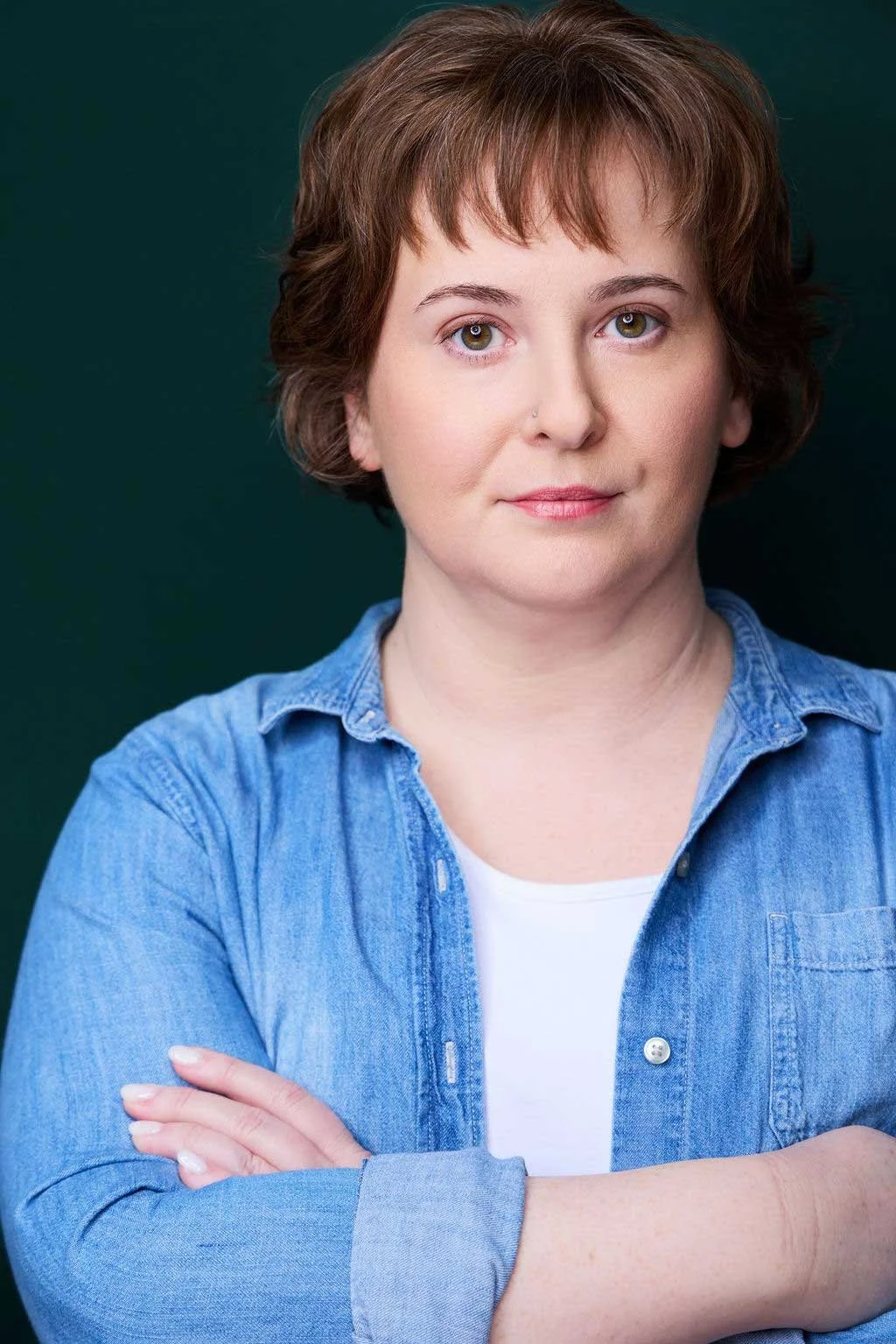 Sue Gauthier has her brown hair down, a serious smirk, and is looking at the camera. Wearing a denim button-down shirt, showing her range as an actress/writer.