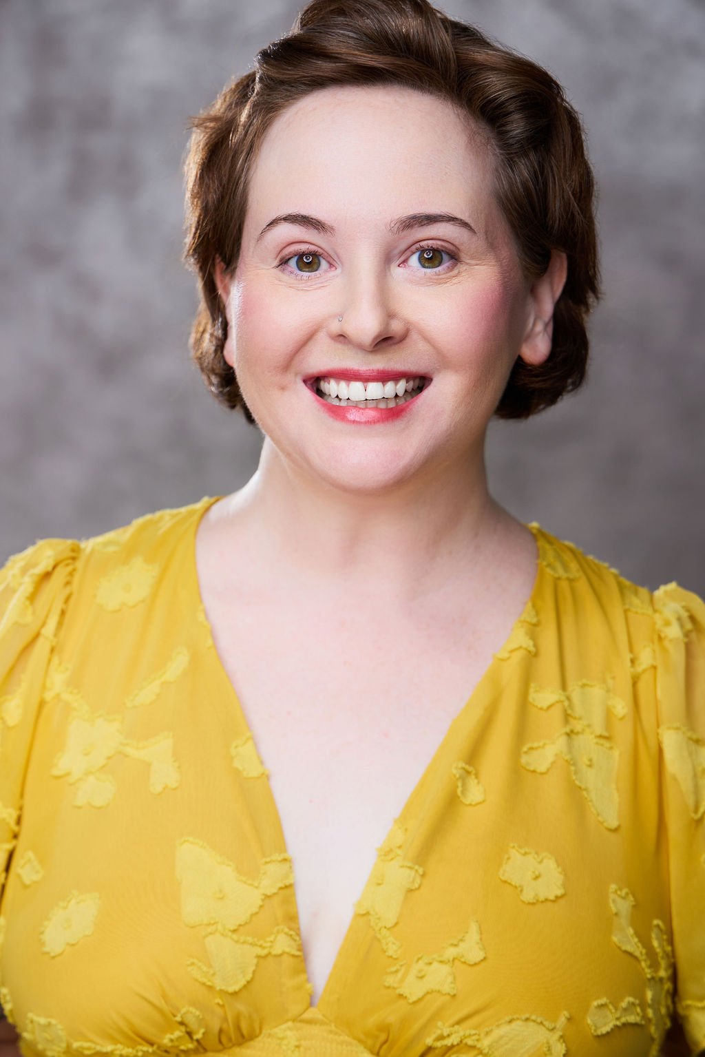 Sue Gauthier is wearing her brown hair down and slightly pinned down, with an open-mouth smile, looking at the camera. Wearing a yellow shirt, showing her range as an actress/writer.