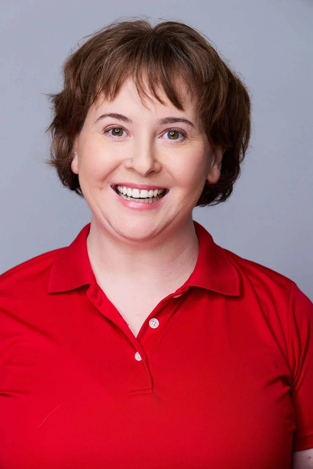 Sue Gauthier has her brown hair down, an open-mouthed smile, looking at the camera. Wearing a red polo shirt, showing her range as an actress/writer.