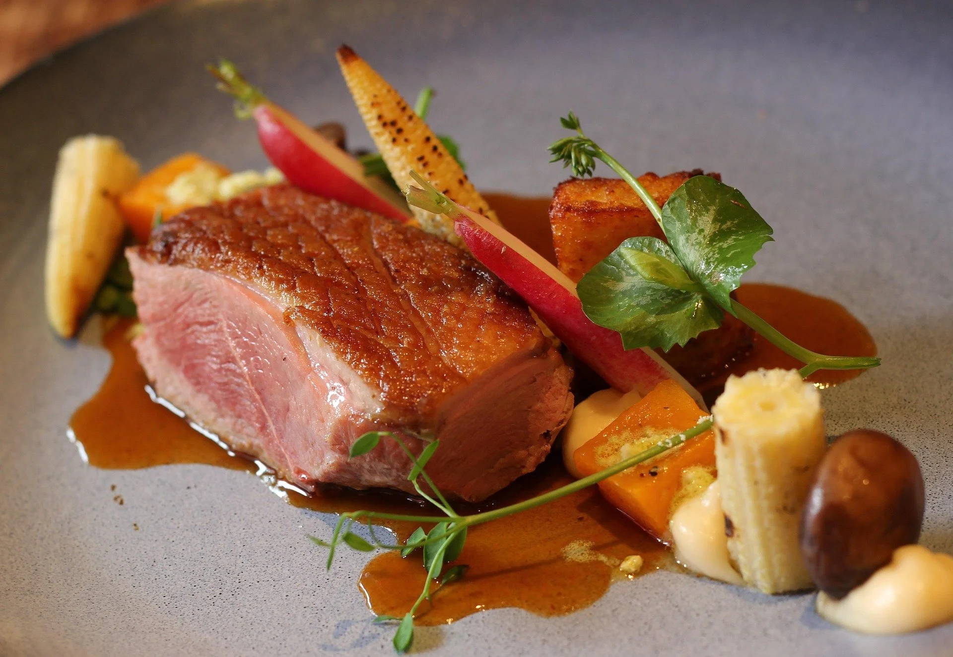 Seared lamb chop with vegetables and sauce on a gray plate.