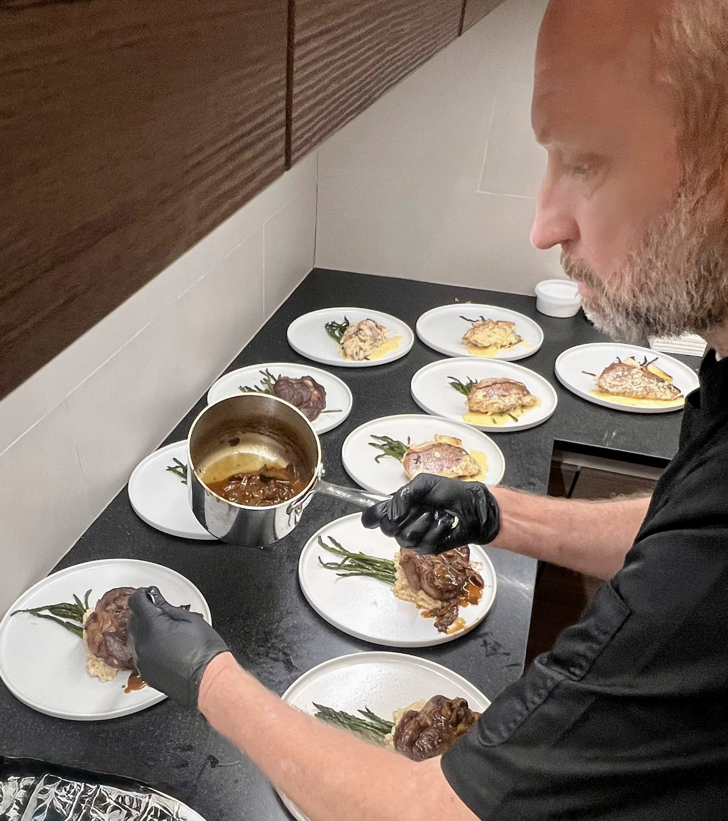 A chef garnishing plates of food with a sauce in a professional kitchen.