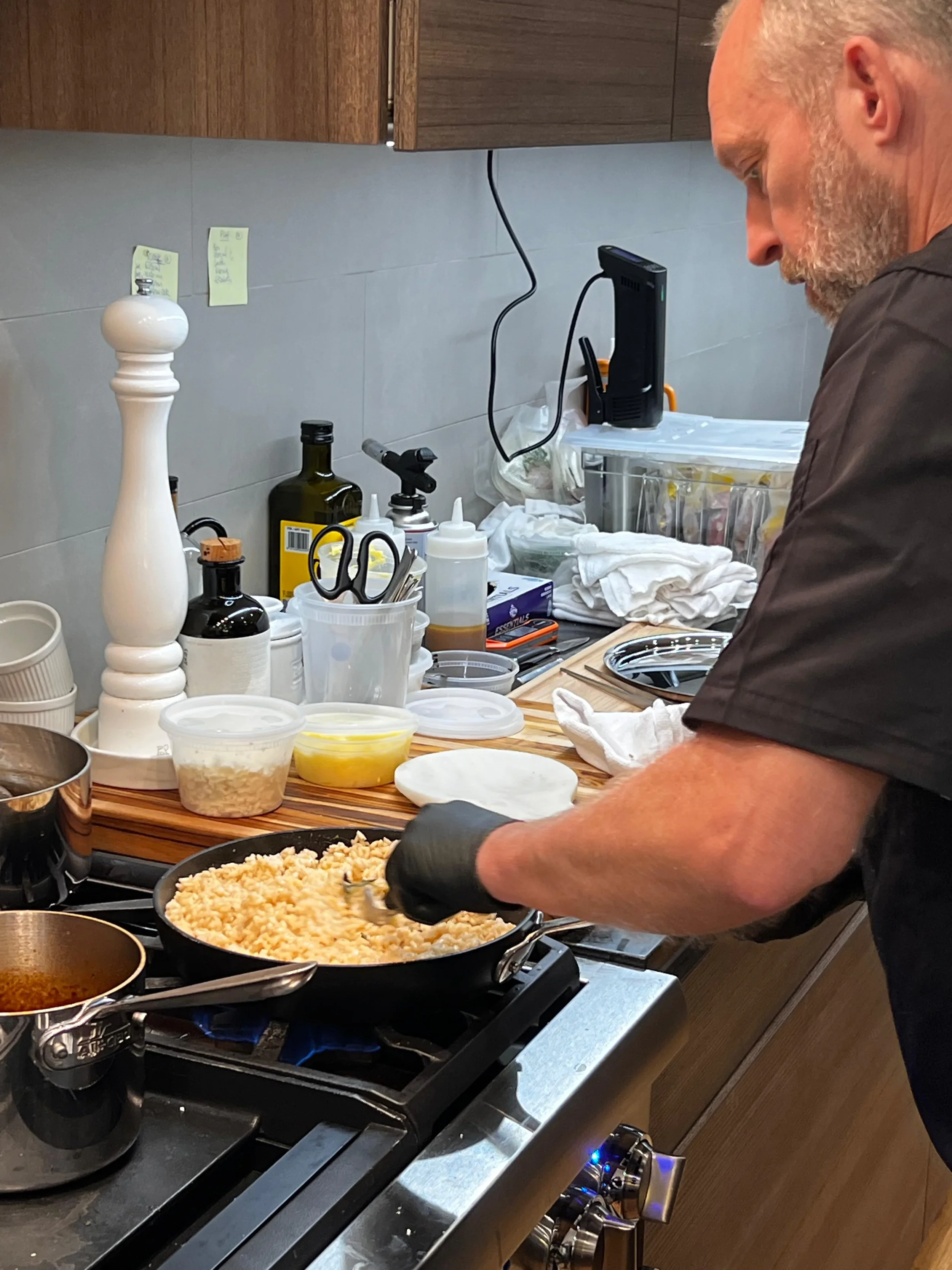 A man cooking rice in a skillet on a stovetop in a cluttered kitchen.