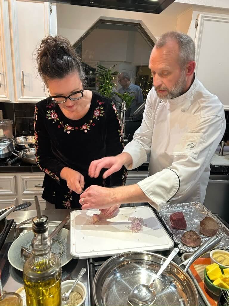 A man and woman cooking together in a kitchen, with the woman assisting the man in preparing food on a cutting board.