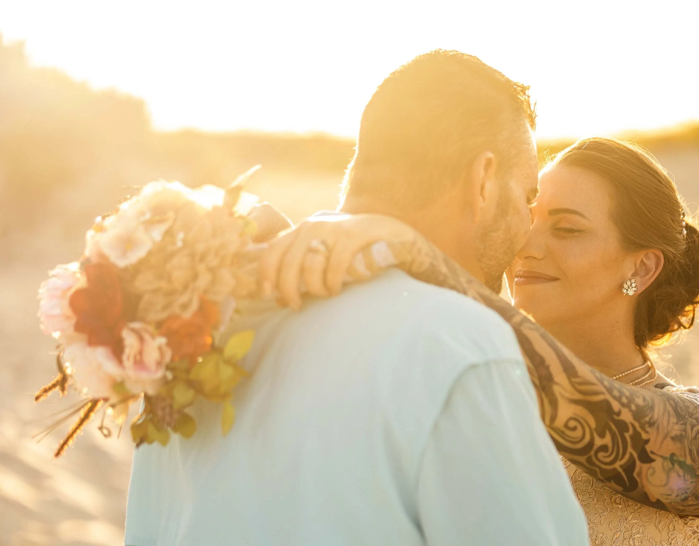 Bride and groom share a romantic kiss during a golden sunset beach wedding ceremony in the Outer Banks officiated by Wedding Knots Tied.