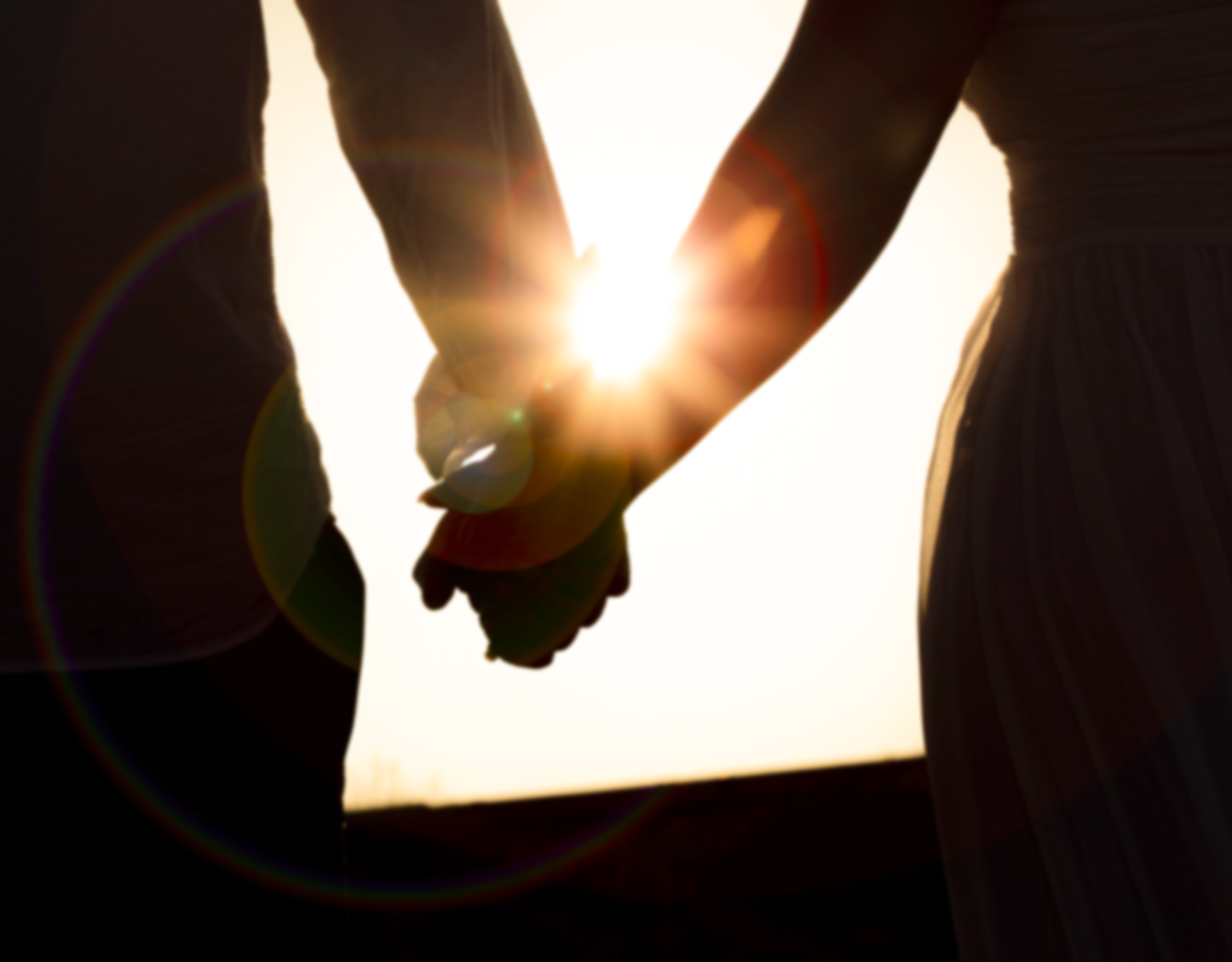 Two people holding hands at sunset, silhouette, sunlight streaming through their hands.