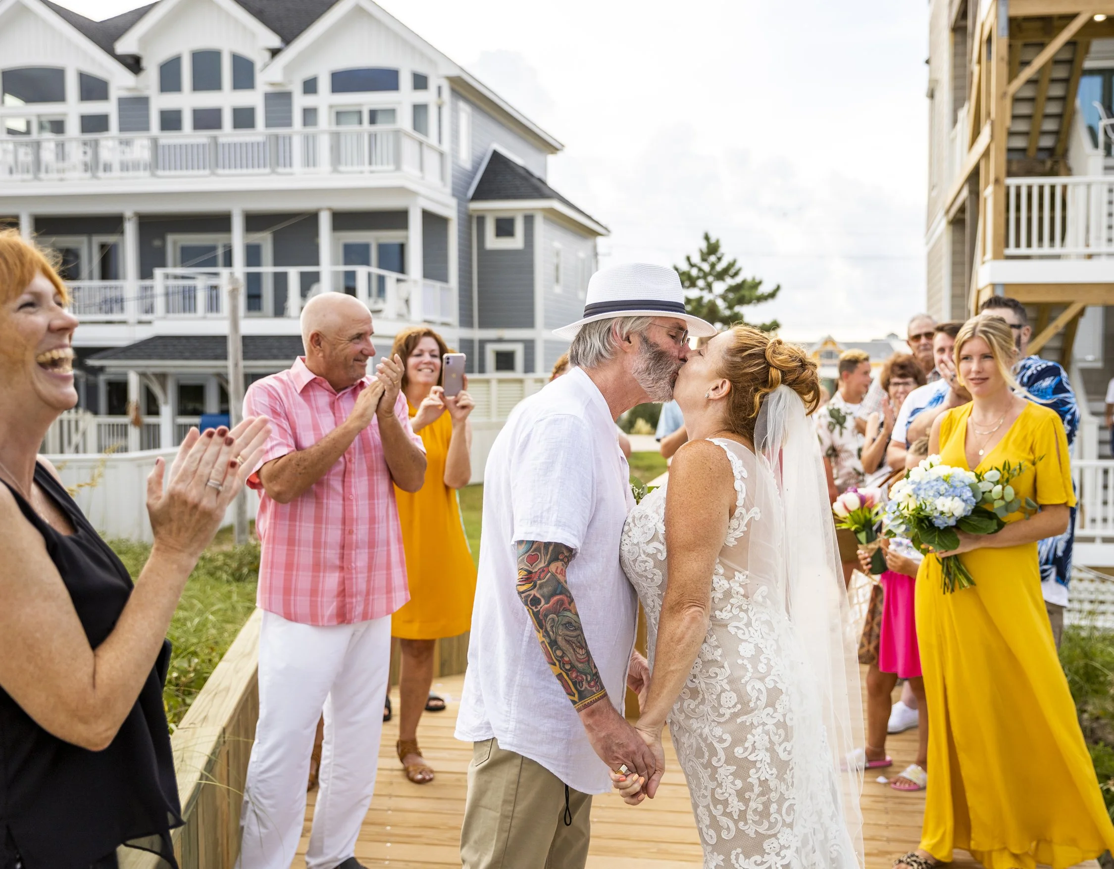 Rev Melody laughing and clapping with the festive wedding party, bride and groom as they kiss